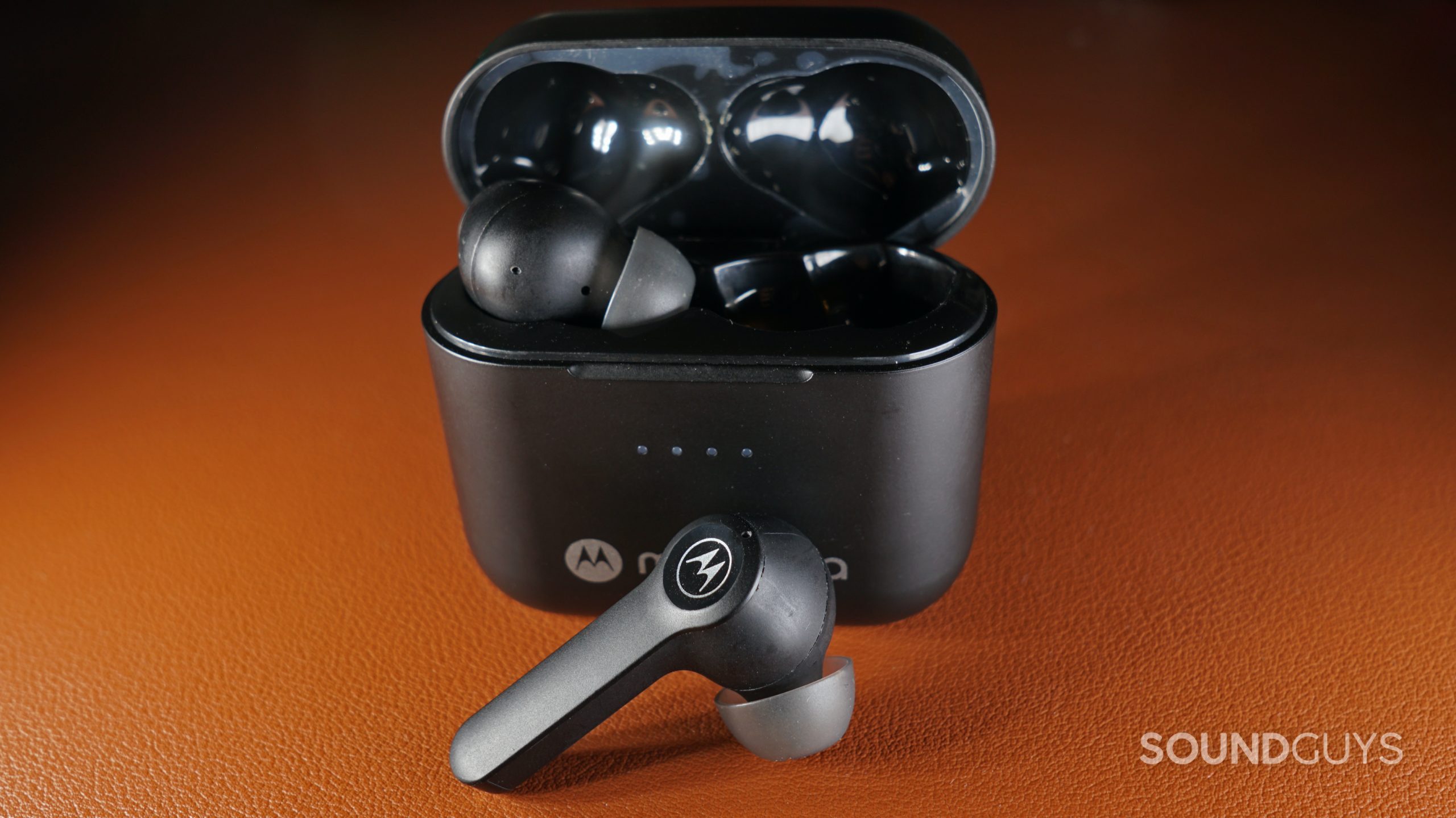 The Motorola Moto Buds-S ANC sits on a leather surface with one earbud out of the charging case.