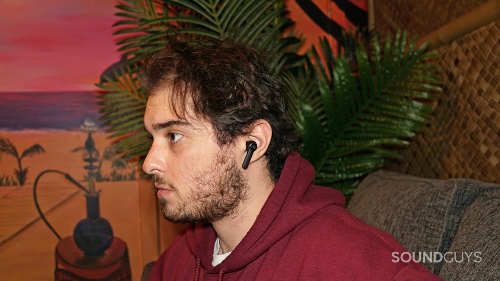 A man sits on a couch wearing the Motorola Moto Buds S ANC.