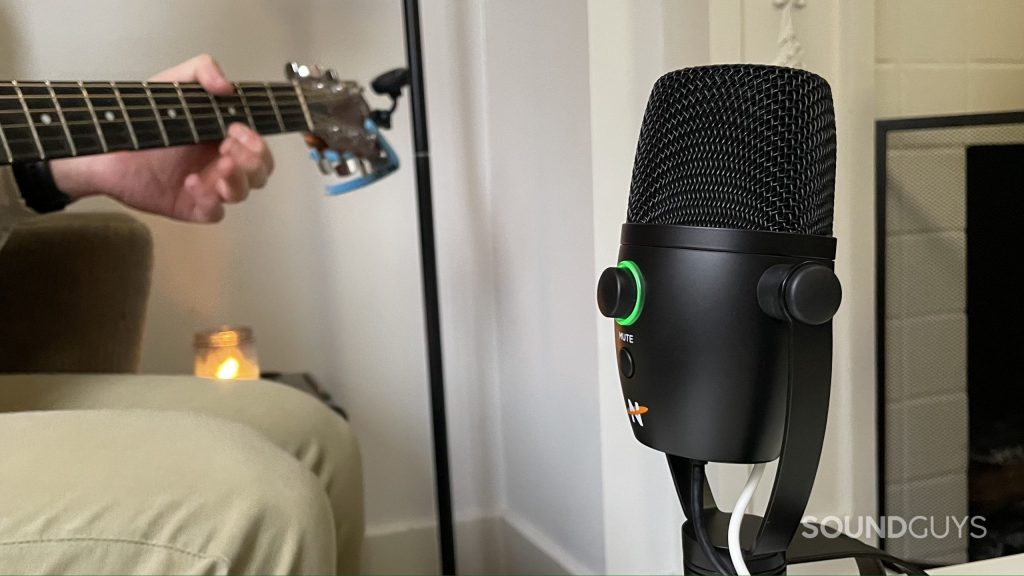 The Neat Bumblebee II with the multifunction button glowing green. A man playing guitar is visible in the background.