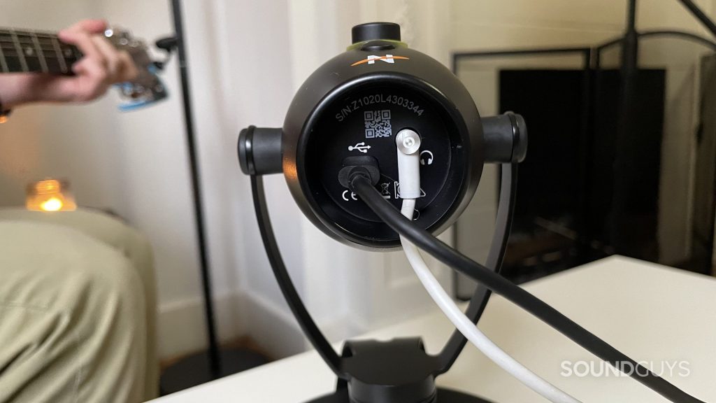 The bottom of the Neat Bumblebee II showing the USB-C port and headphone port. A man playing guitar is visible in the background.