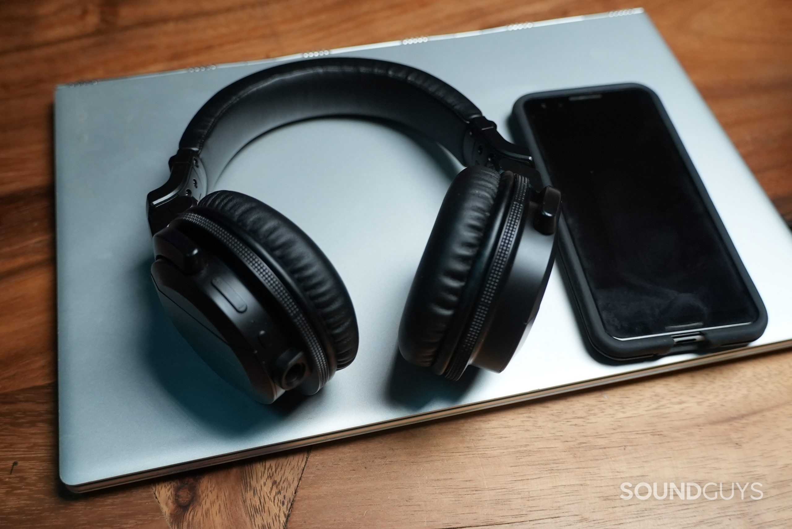 The Pioneer HDJ-CUE1BT lying on a closed silver laptop next to a smartphone on its left.