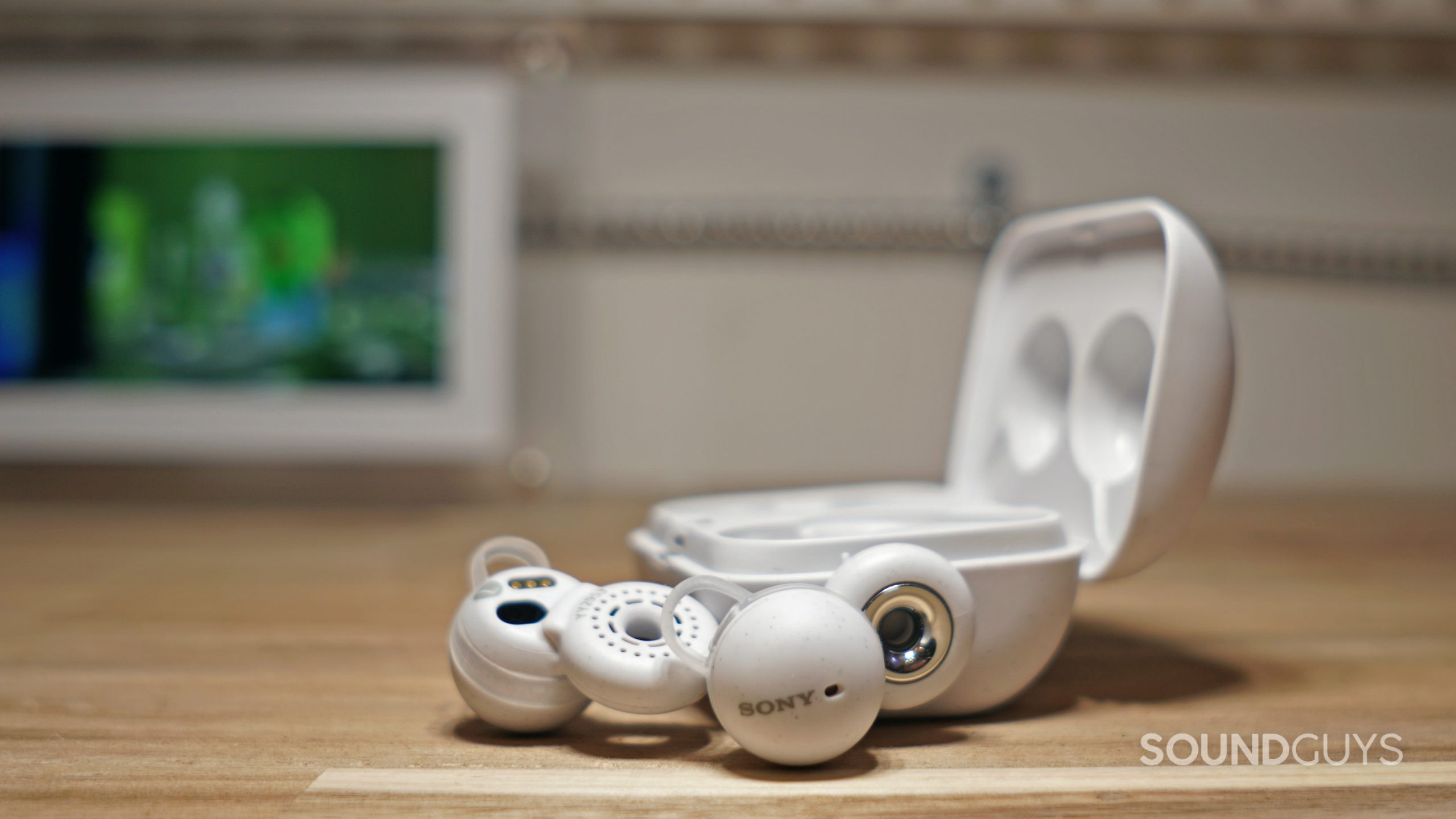 The Sony LinkBuds earbuds lay on a wooden surface next to their open charging case.