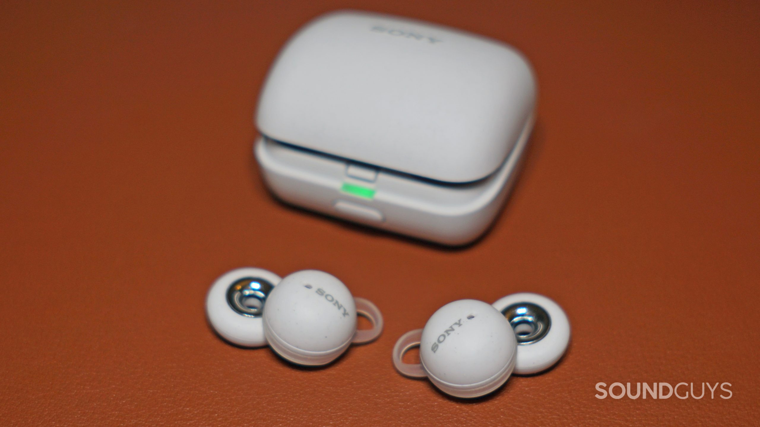 The Sony LinkBuds earbuds lay on a leather surface in front their charging case.