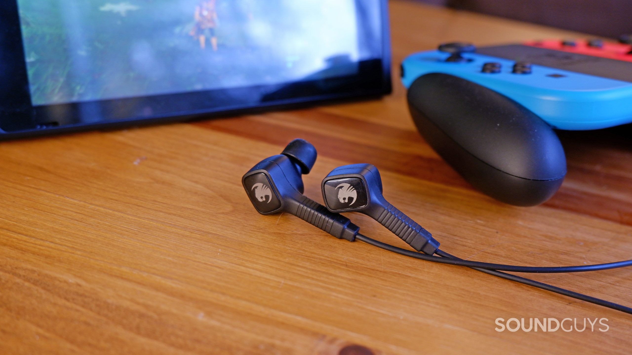 The ROCCAT Syn Buds Core on a wooden table in front of a Nintendo Switch and controller.