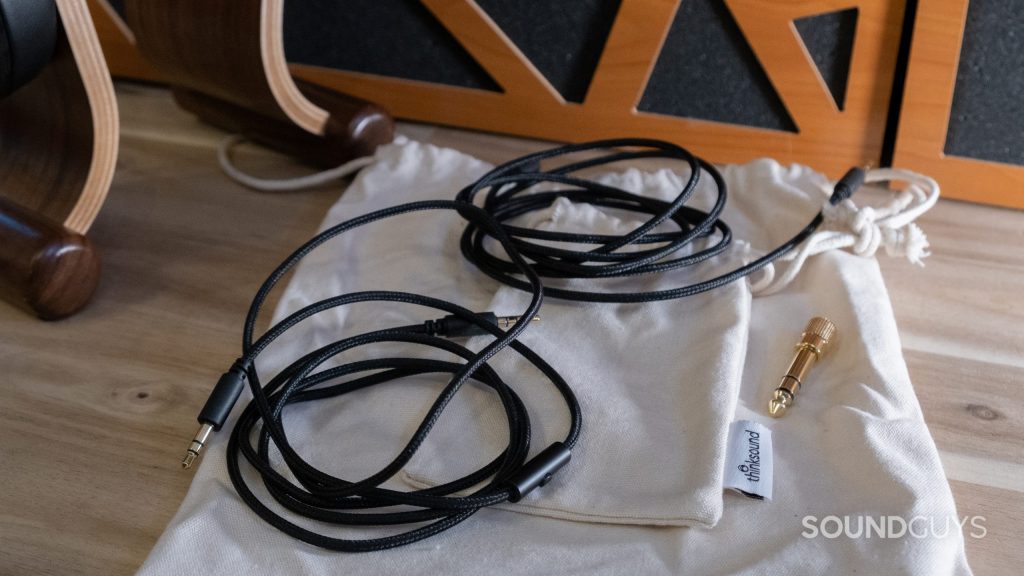 Two cables, two cotton pouches, and a 1/4" adapter that ship with Thinksound ov21 rest on a wood surface.