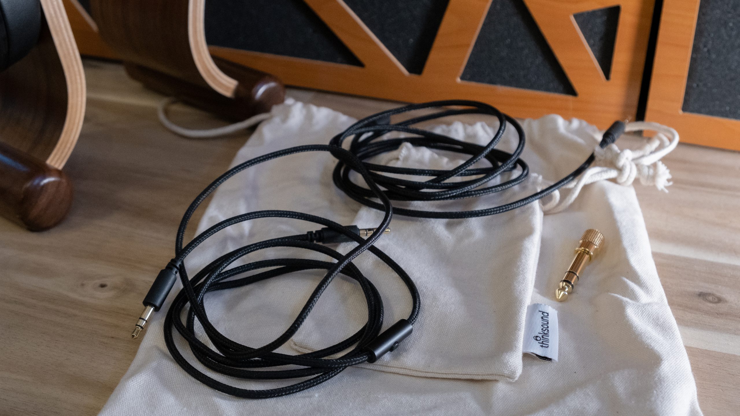Two cables, two cotton pouches, and a 1/4&quot; adapter that ship with Thinksound ov21 rest on a wood surface.