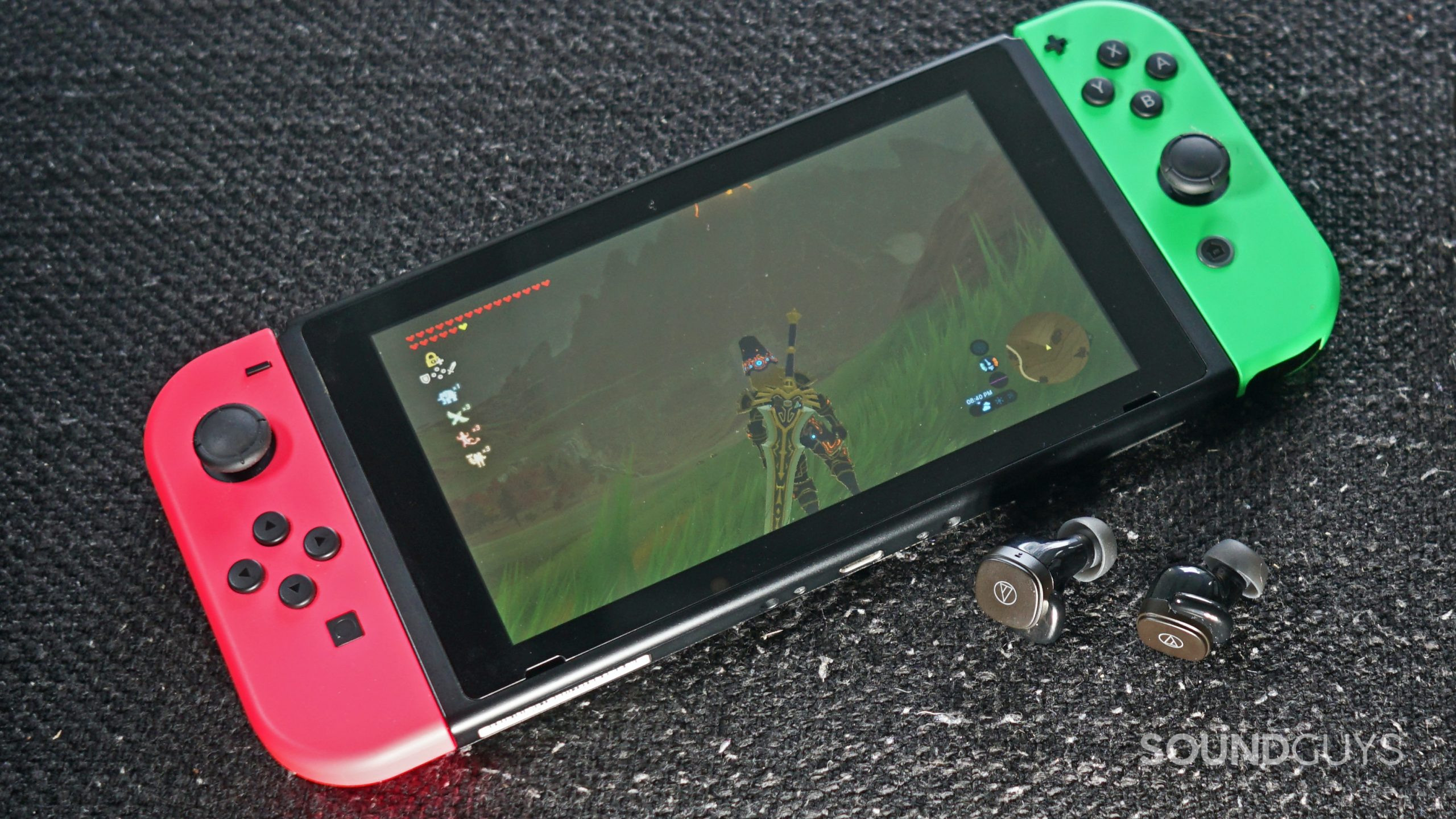 The Audio-Technica ATH-SQ1TW true wireless earbuds lay on a fabric surface next to a Nintendo Switch running Legend of Zelda Breath of the Wild.