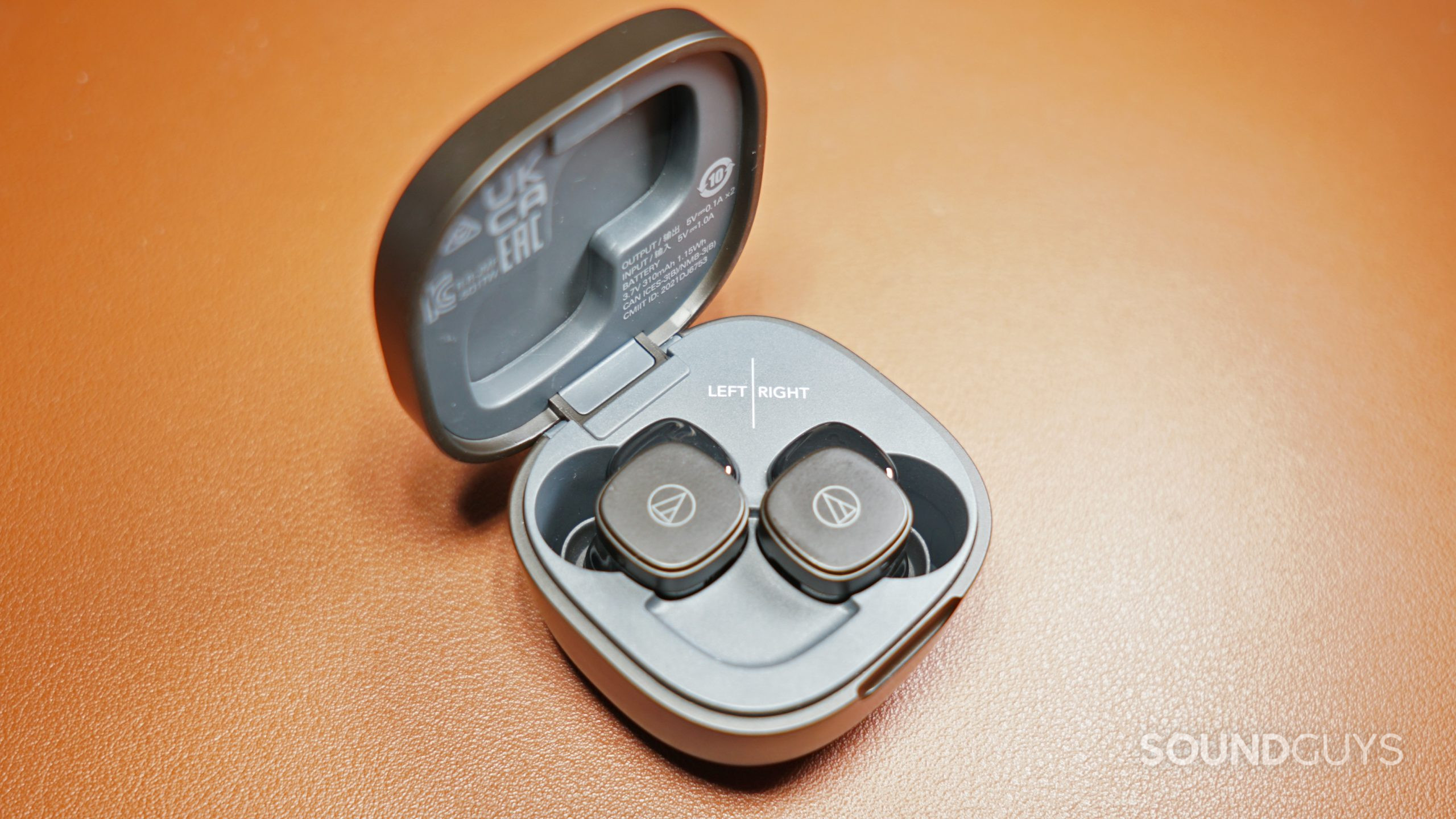 The Audio-Technica ATH-SQ1TW sits in its charging case on a leather surface