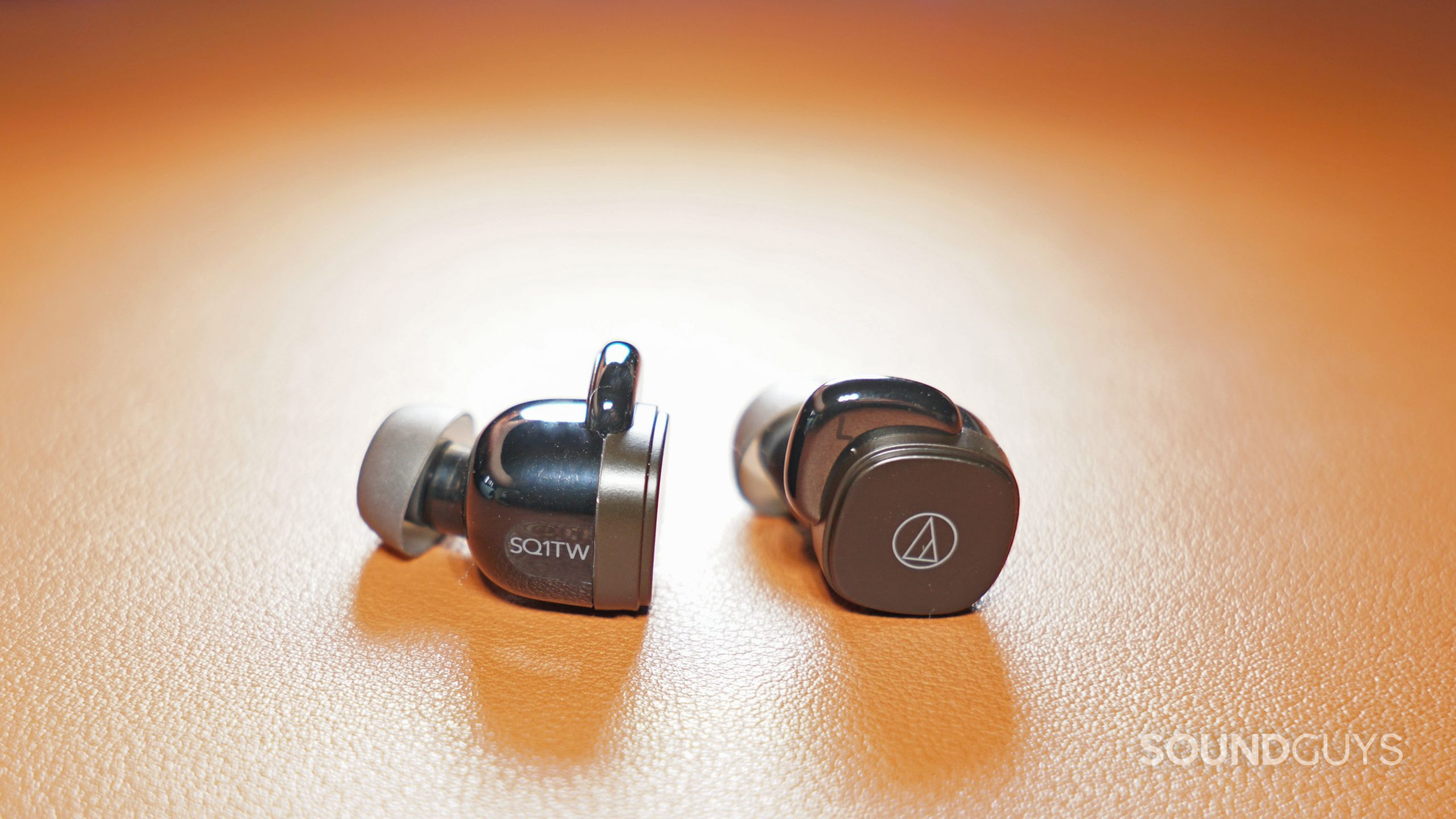 The Audio-Technica ATH-SQ1TW lay on a leather surface.