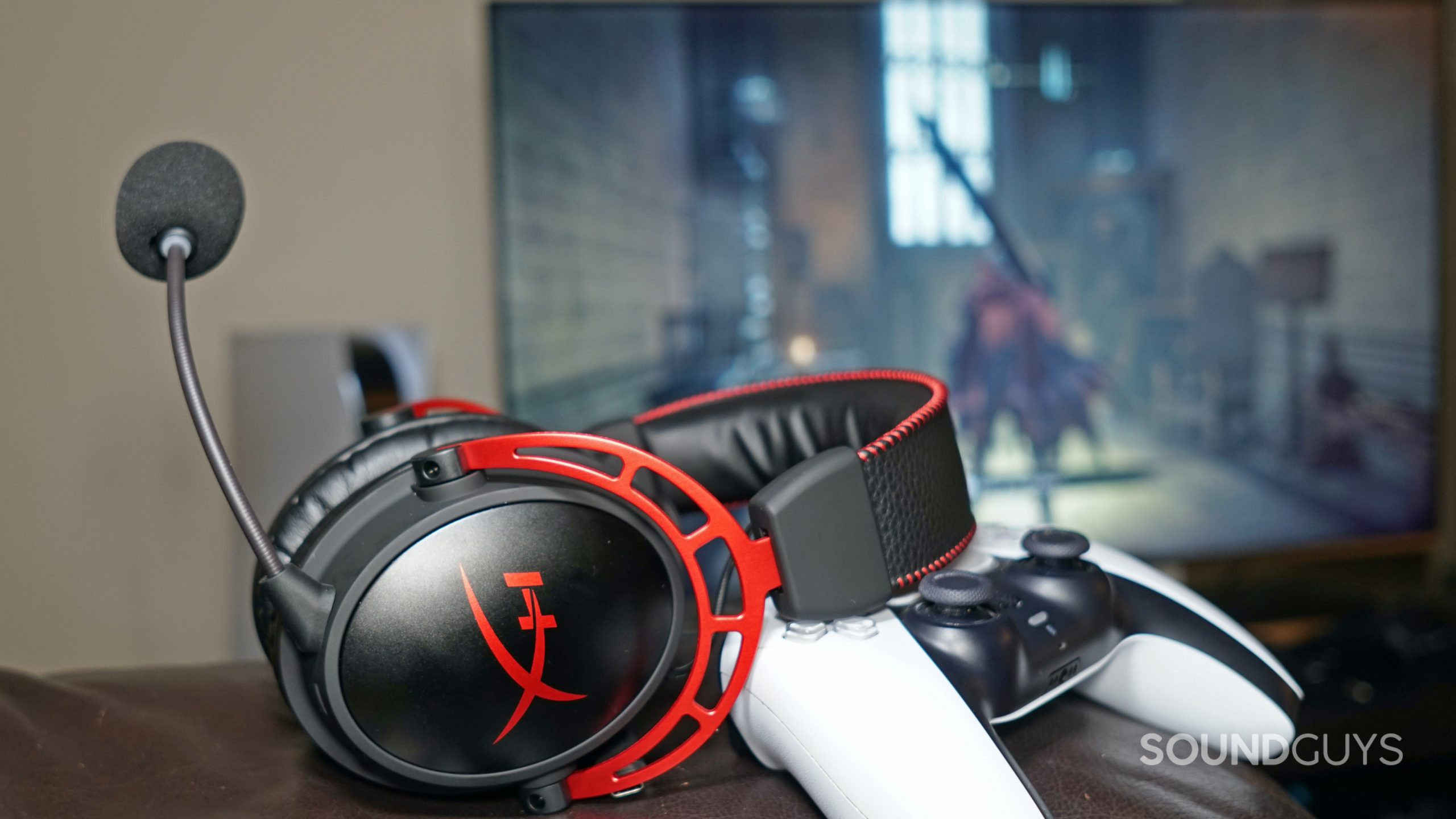 The HyperX Cloud Alpha Wireless leans on a PlayStation DualSense controller on a leather couch, with a PlayStation 5 console standing next to a TV displaying Elden Ring in the background.