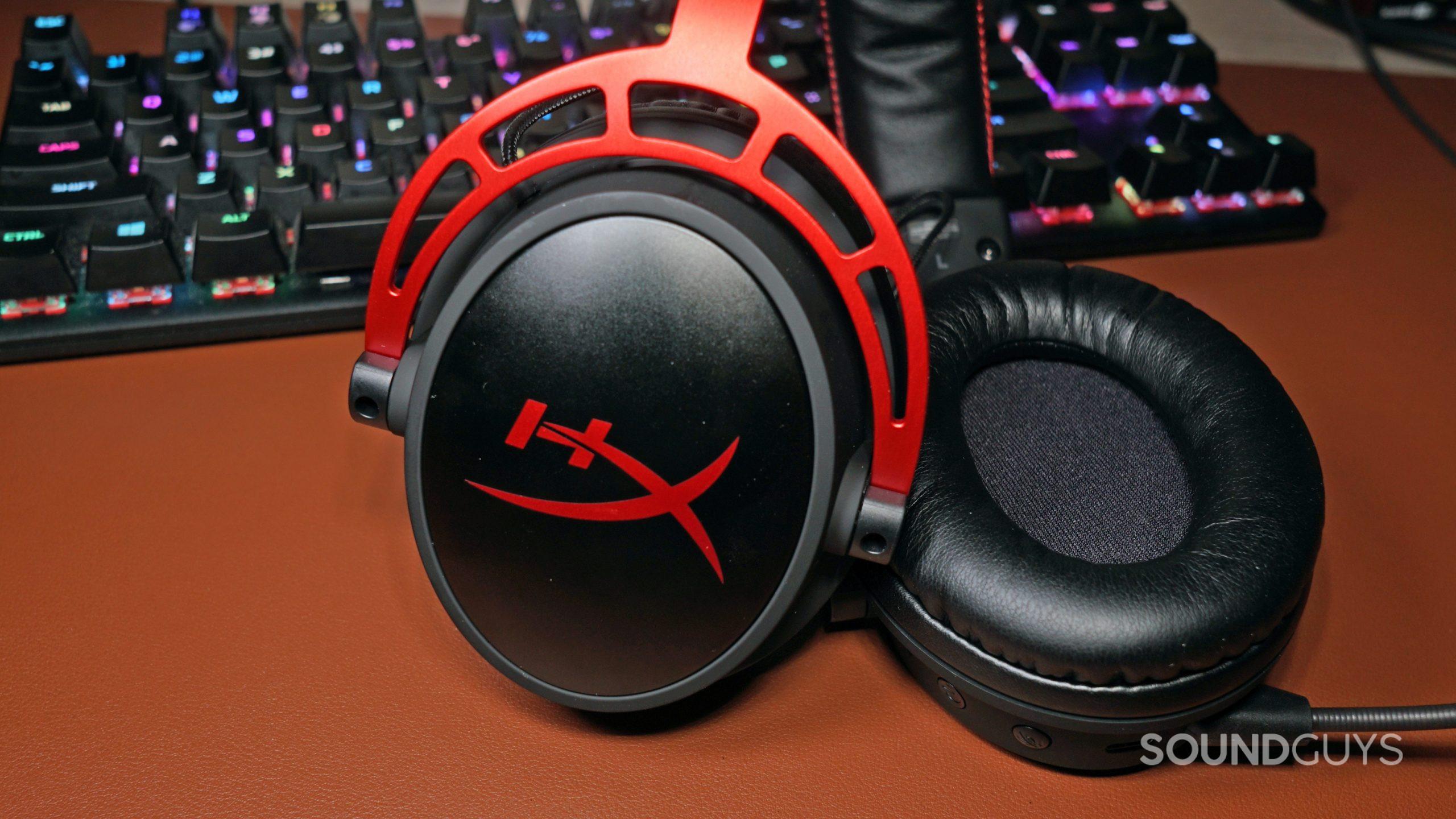 The HyperX Cloud Alpha Wireless gaming headset lays on a leather surface in front of a HyperX mechanical gaming keyboard.