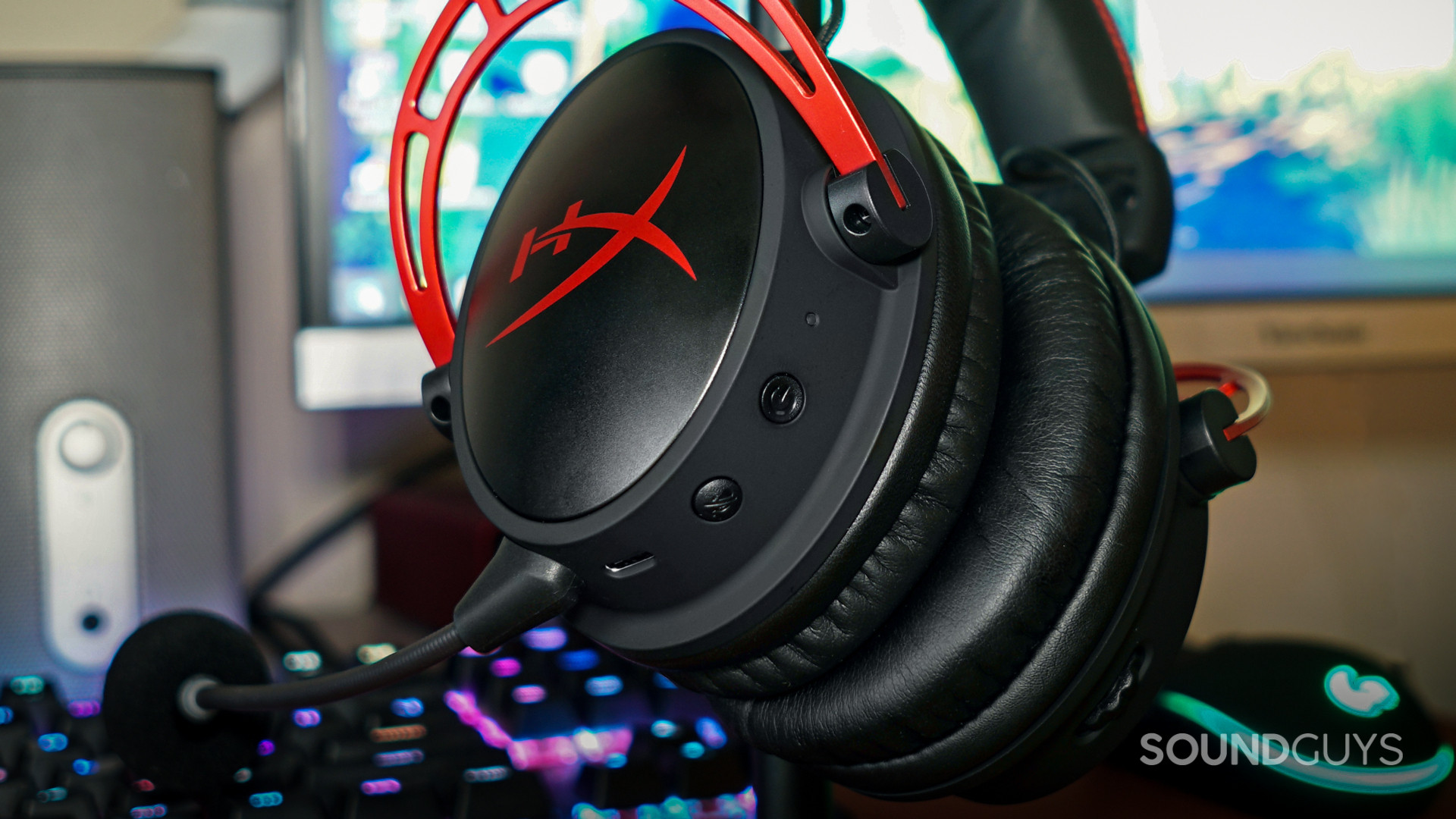 The HyperX Cloud Alpha Wireless sits on a headphone stand in front of a gaming PC.