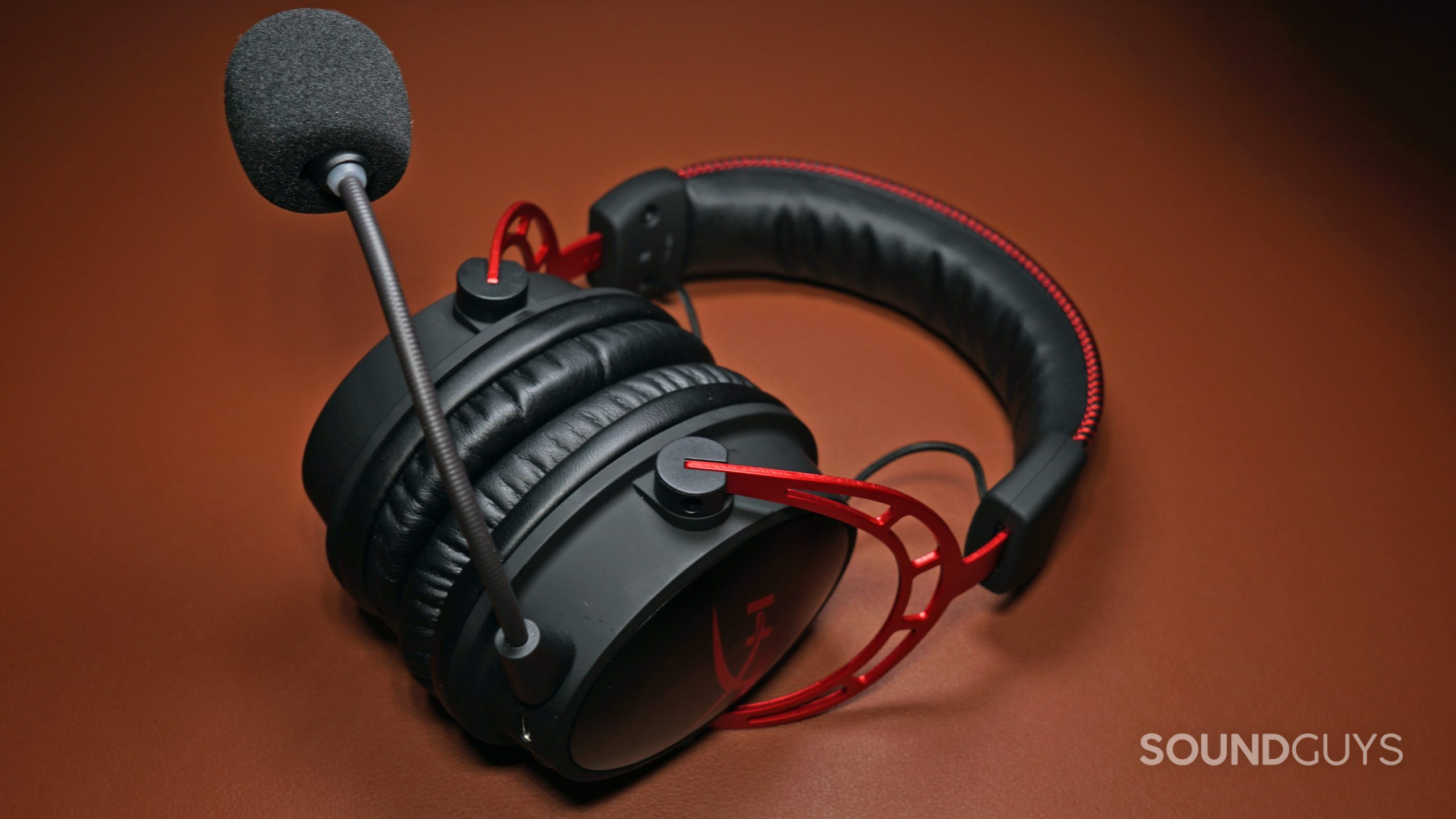 The HyperX Cloud Alpha Wireless lays on a leather surface with its boom mic attached.