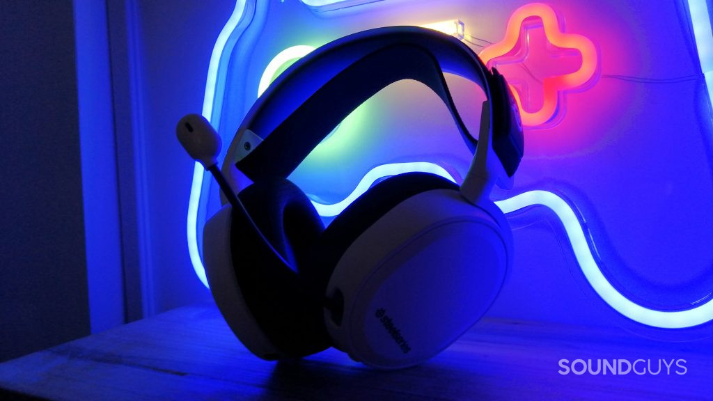 SteelSeries Arctis 7P+ Wireless leans against a neon sign.
