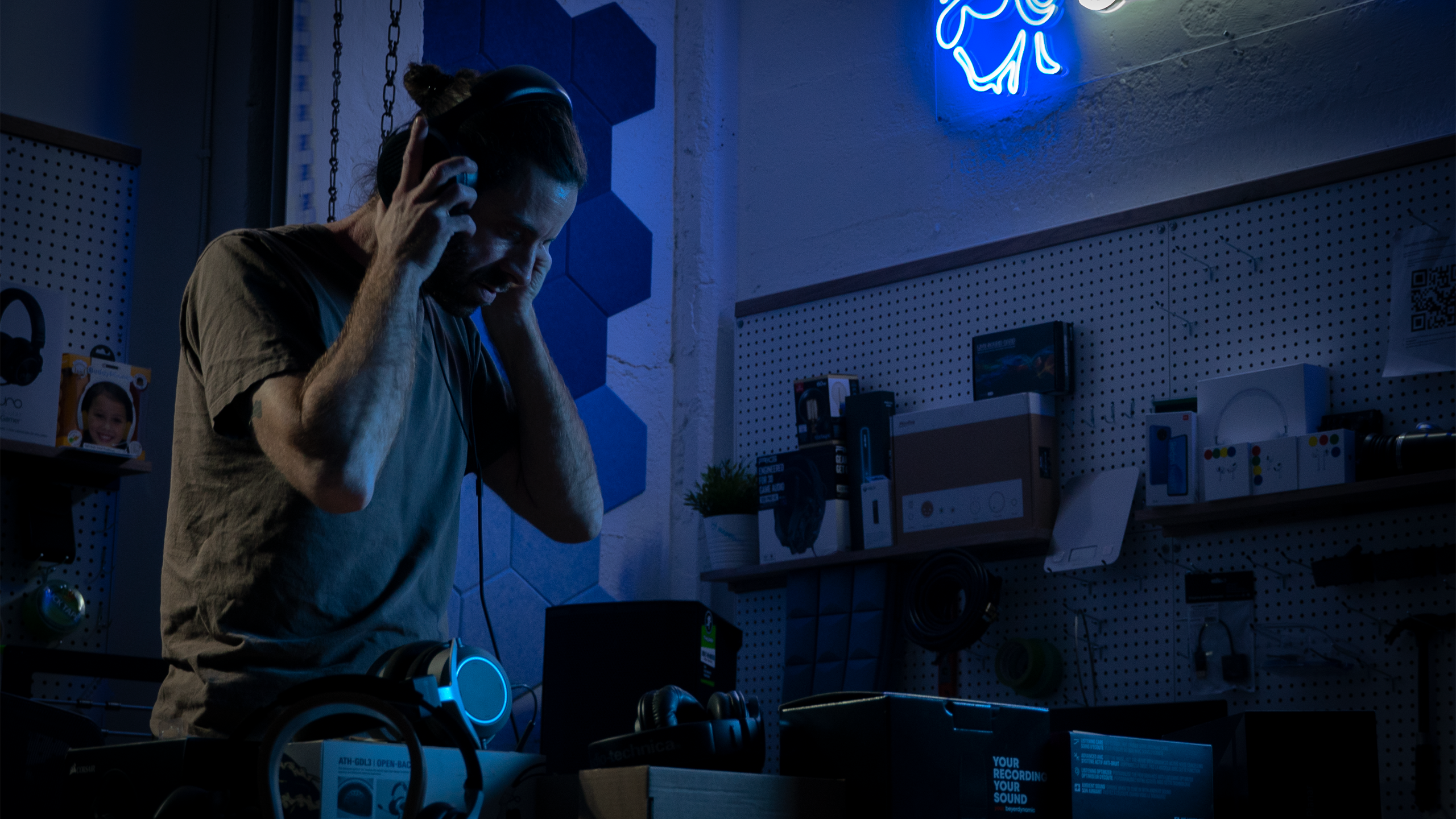 A photo of AJ Wykes listening to headphones in a dark room.