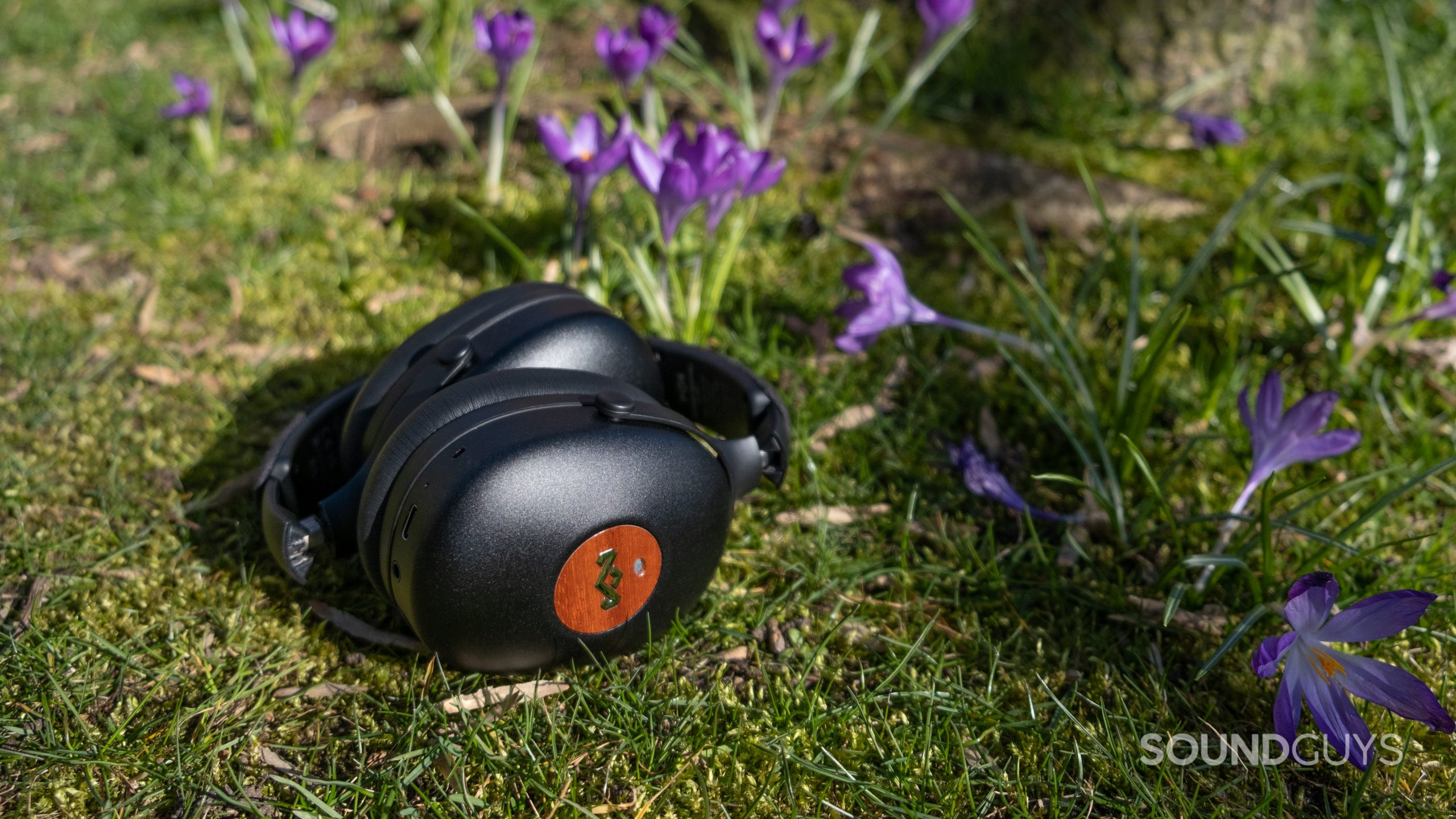 House of Marley Positive Vibration XL ANC folded up on a bed of grass with purple flowers.