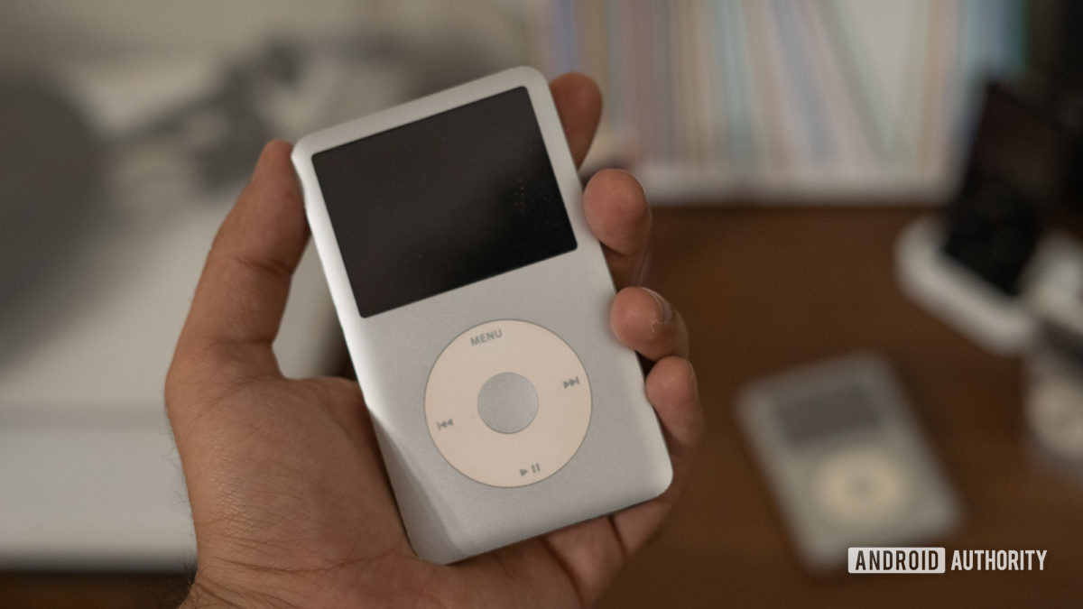 A hand holds the iPod Classic (silver).
