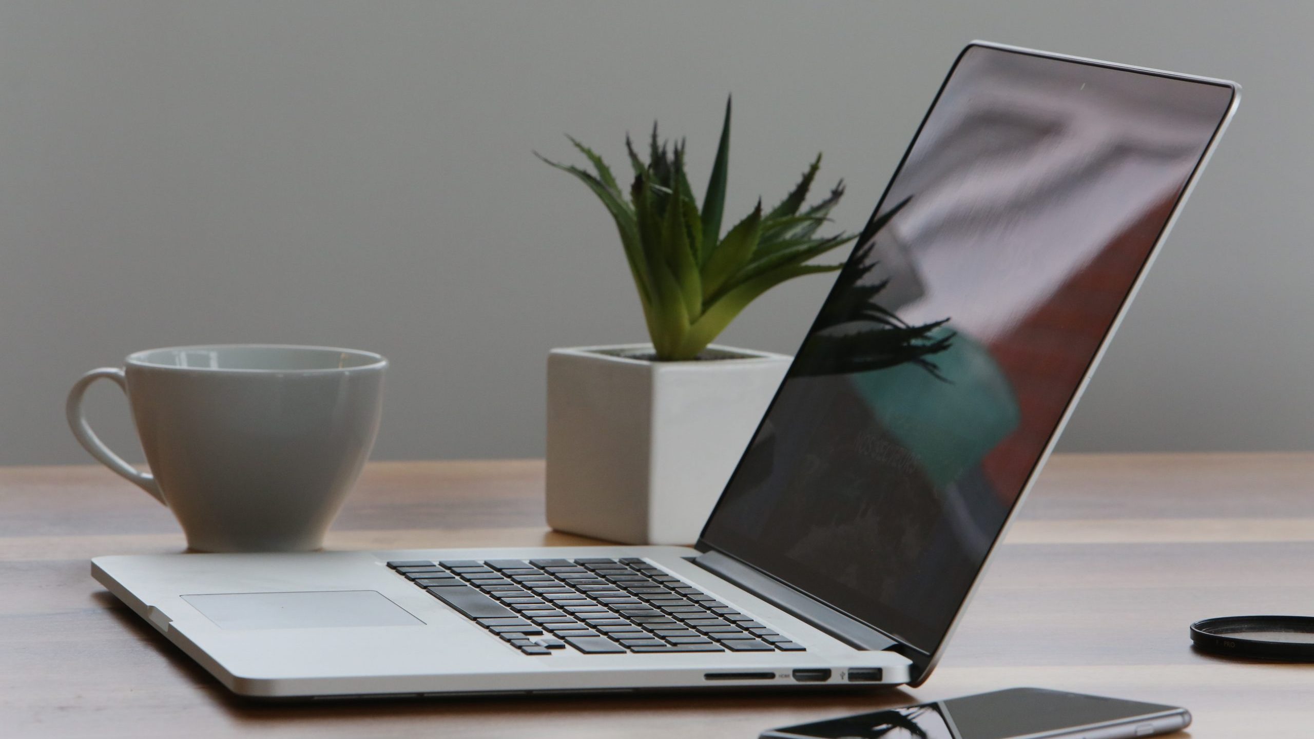 A laptop rests on a desk near a smartphone, cup of coffee, and small plant.