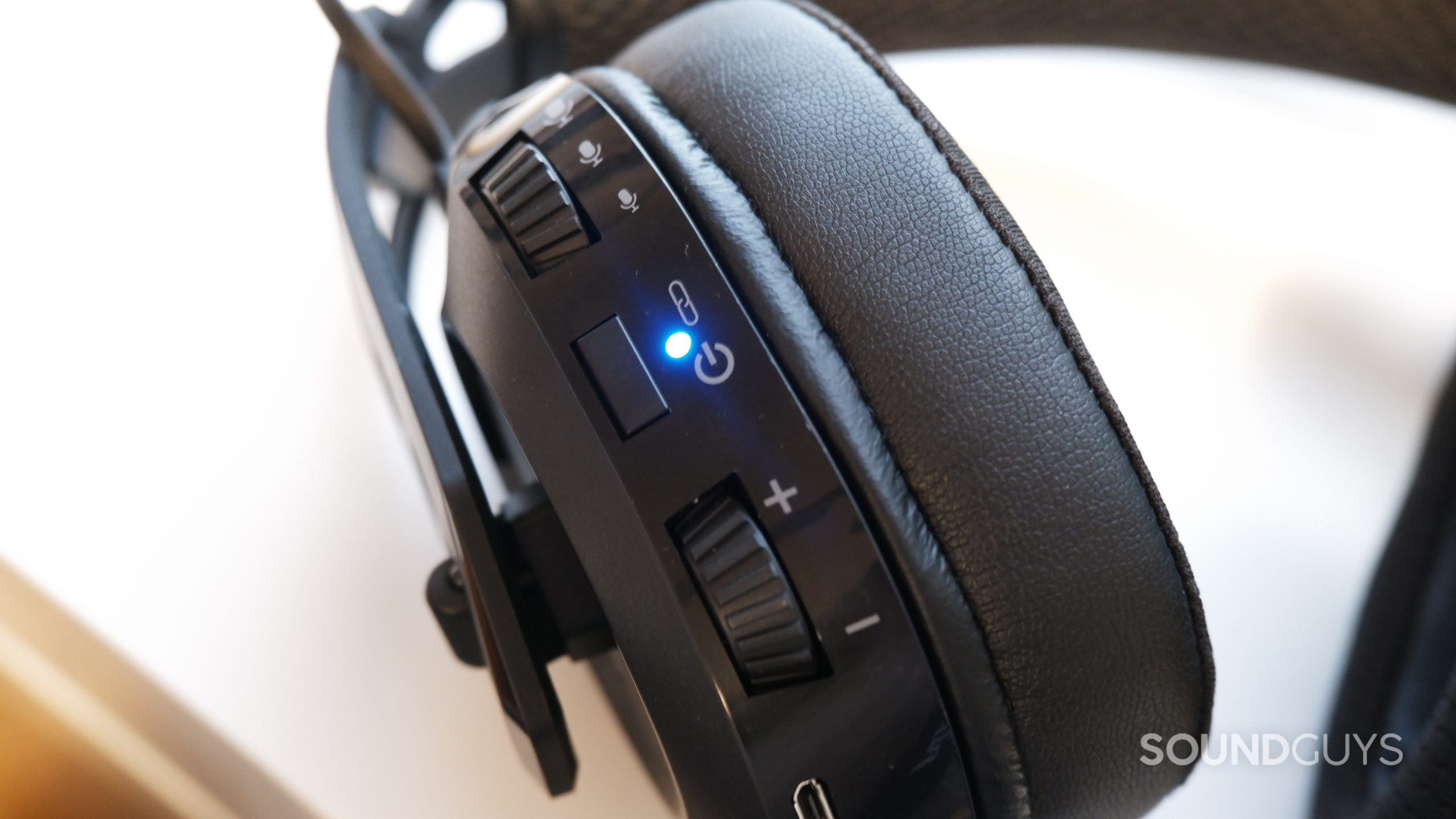 A close-up of the left ear cup on the RIG 700 PRO HS, showing the volume and microphone controls, as well as the on button, with the blue &quot;on&quot; light turned on.