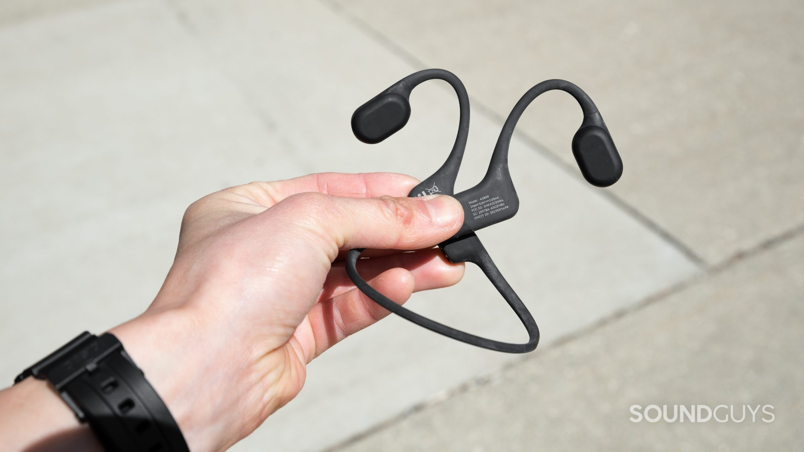 A hand holds the Aftershokz Aeropex bone conduction headphones to show the flat interior of each ear piece.