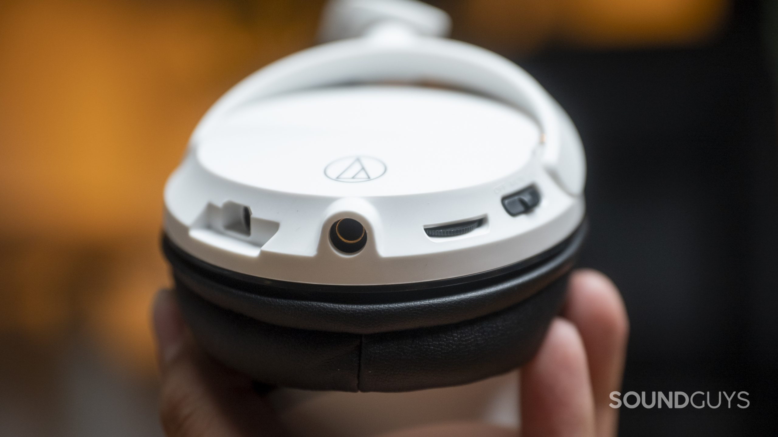 A hand holds the Audio-Technica ATH-GL3 gaming headset to display its ports, dials, and switches.