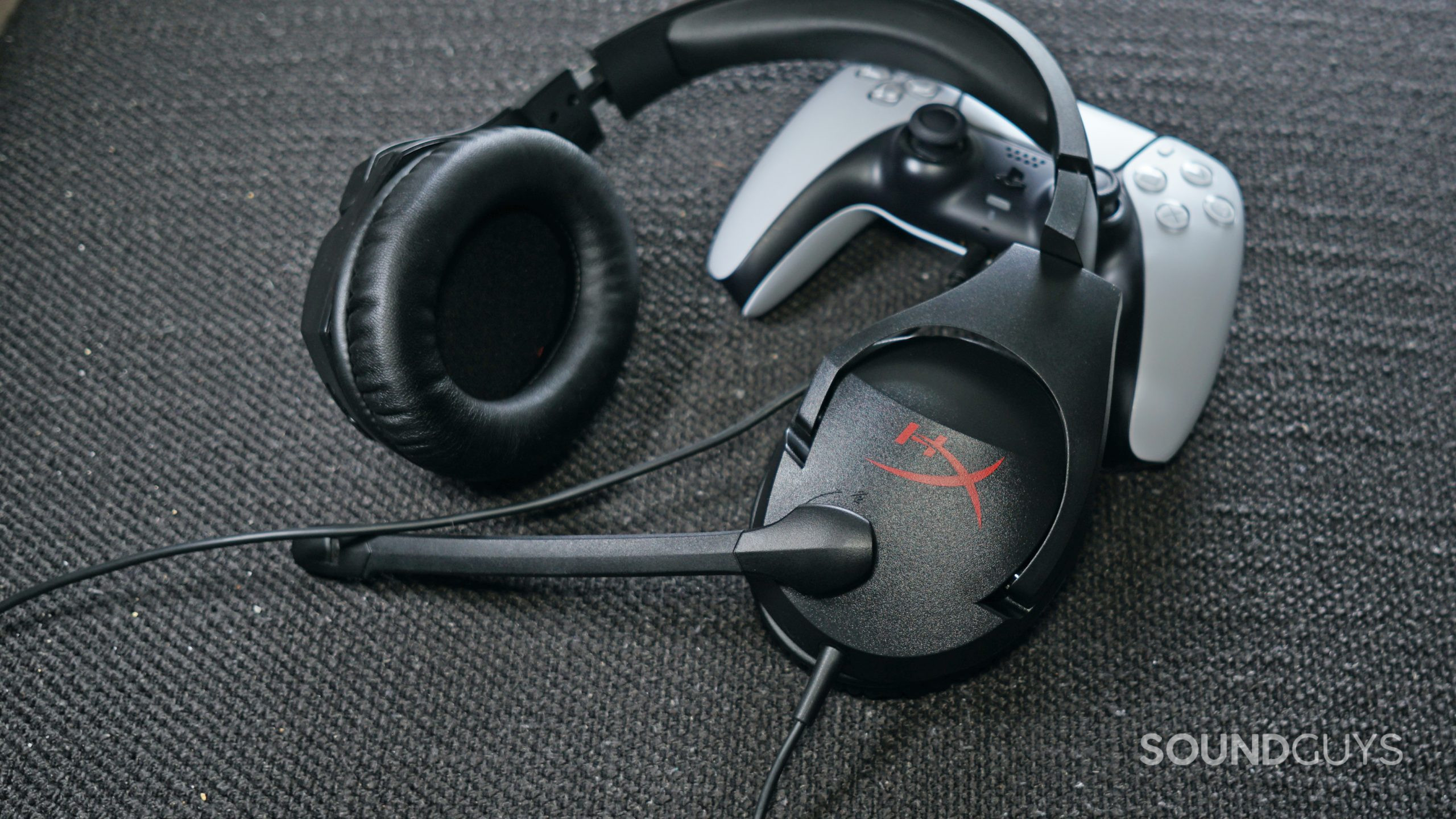 The HyperX Cloud Stinger gaming headset leans on a PlayStation DualSense controller it's plugged into.