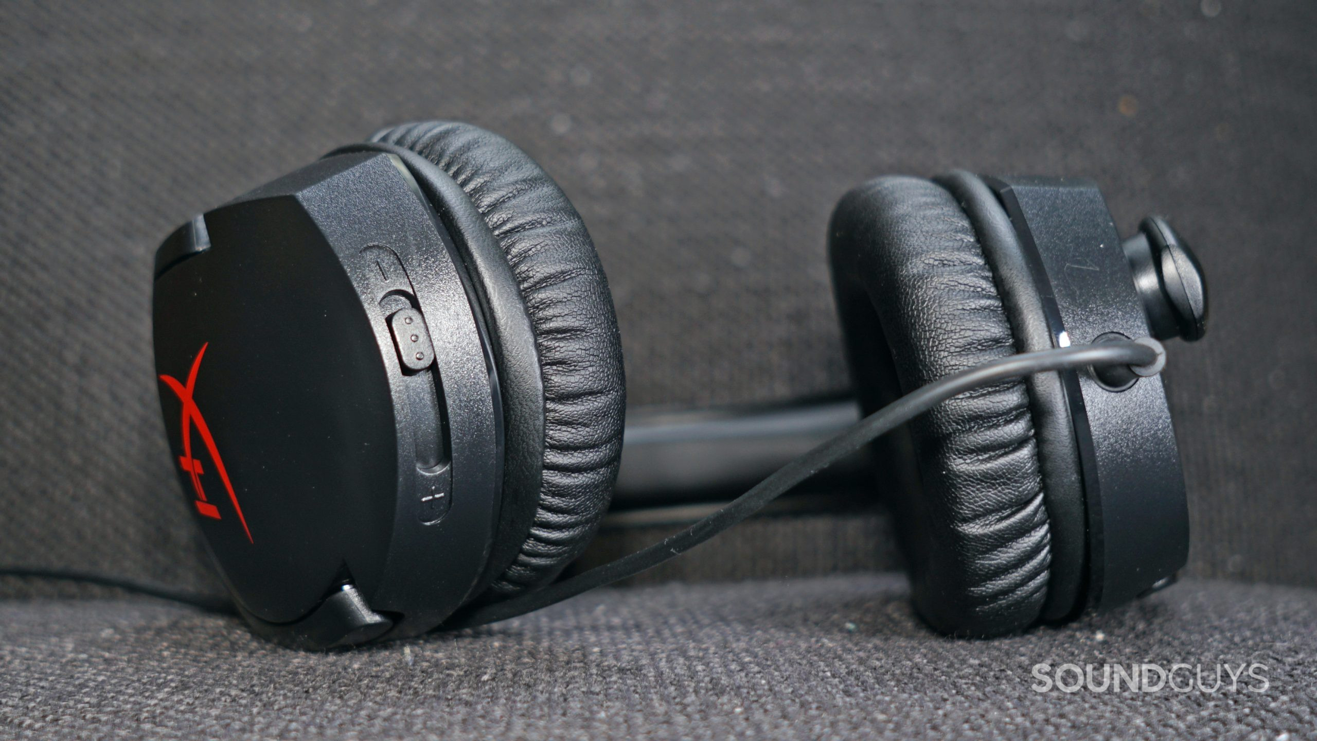 The HyperX Cloud Stinger lays on a fabric surface with the focus on its volume dial.