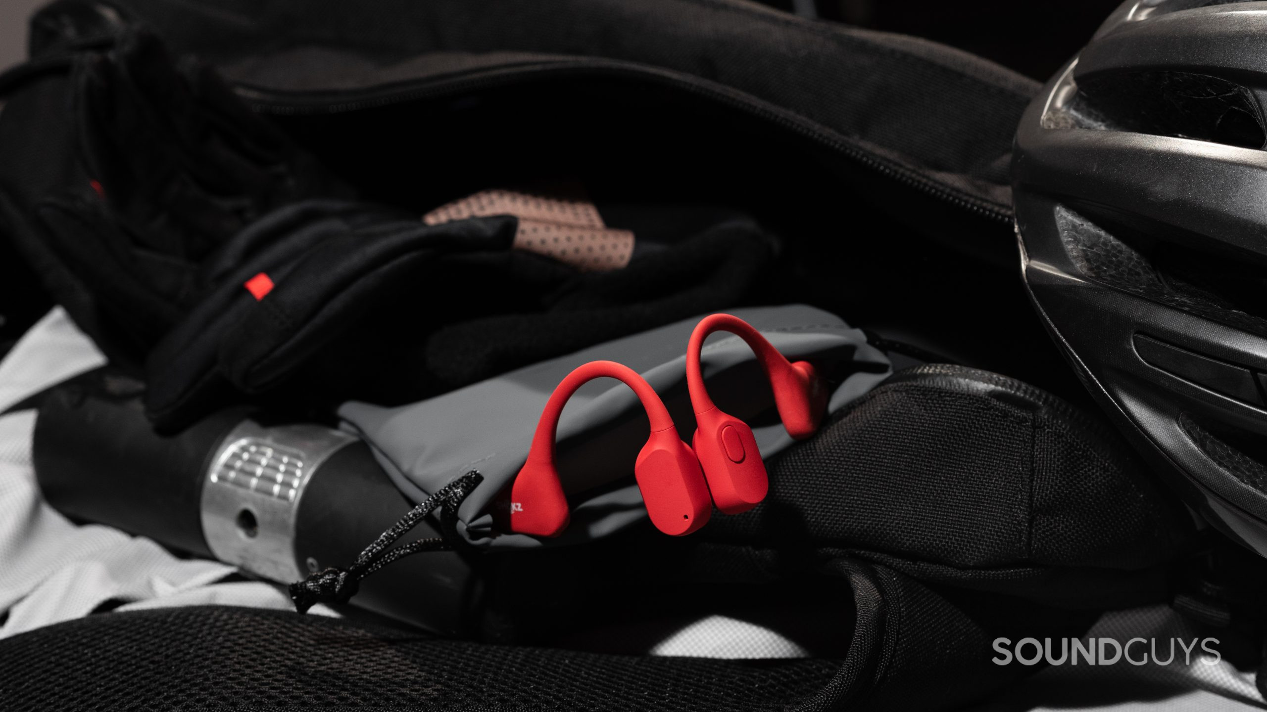 The Shokz OpenRun bone conduction headphones rest in the drawstring carry pouch inside of a sling bag near biking accessories.