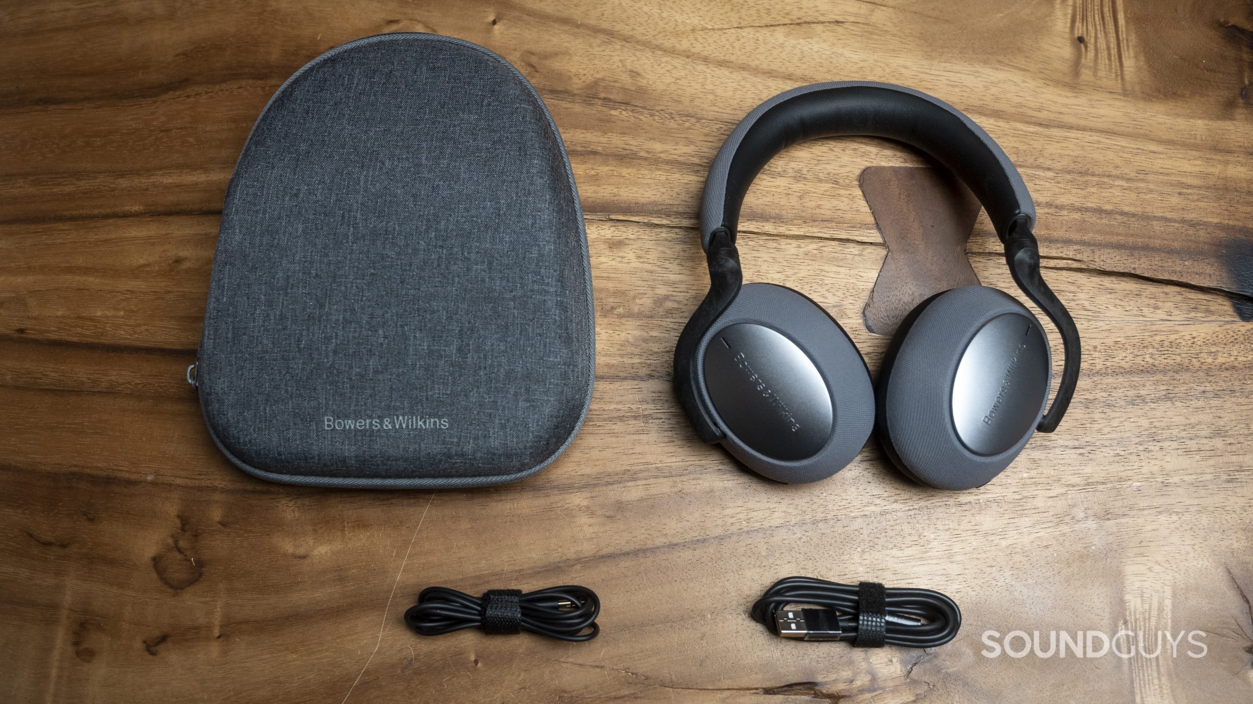 The Bowers &amp; Wilkins PX7 sitting on a wooden table, with the case, headphones, USB-C cable, and 3.5mm cable visible.
