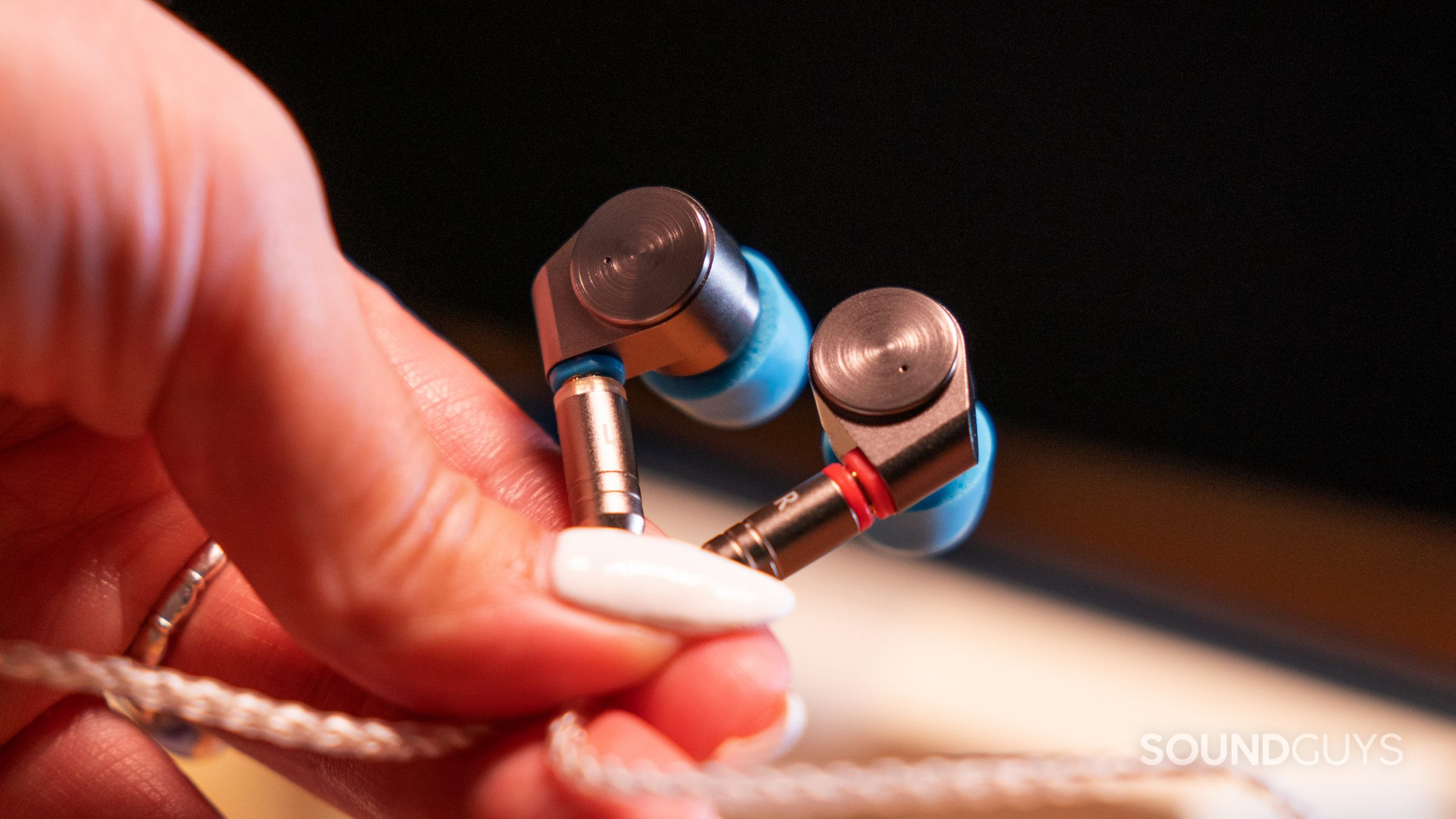 A woman's hand with long nails holds the Linsoul TIN Audio T2 buds at a close up.
