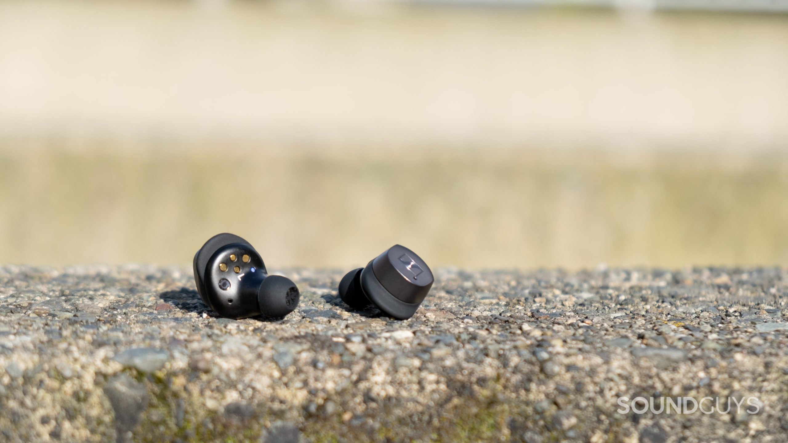 The Sennheiser MOMENTUM True Wireless 3 earbuds rest on rough concrete, showing the inside and outer housings.
