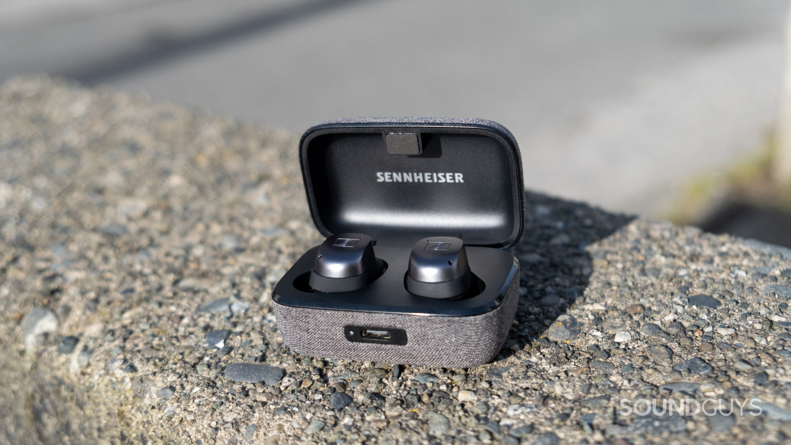 The Sennheiser MOMENTUM True Wireless 3 sits open on rough concrete outside.