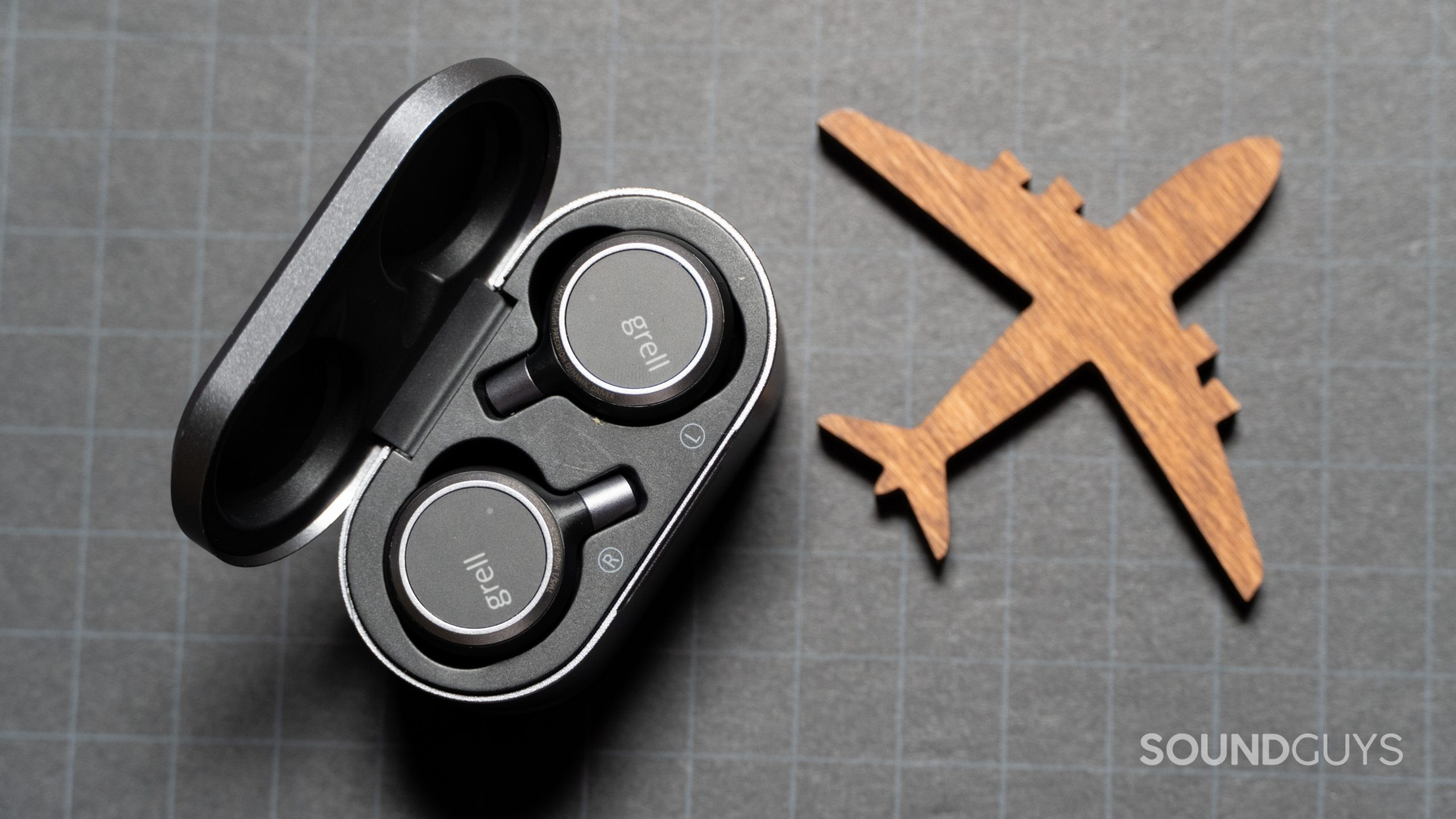 Grell Audio TWS 1 earbuds in case next to a paper airplane cutout.