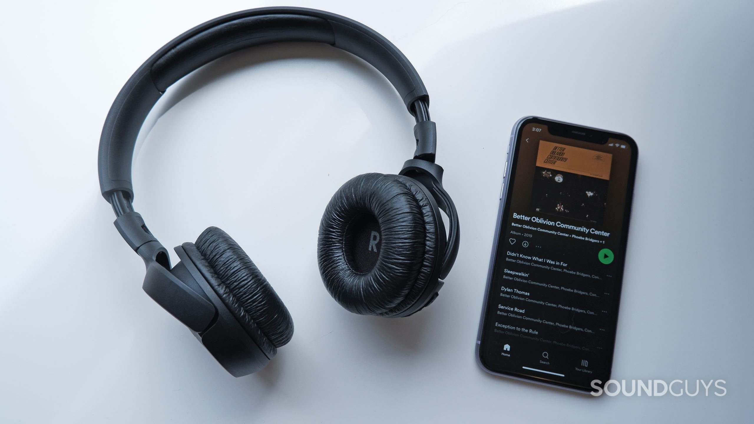 The JBL Tune 510BT on a white table next to a phone with Spotify open.