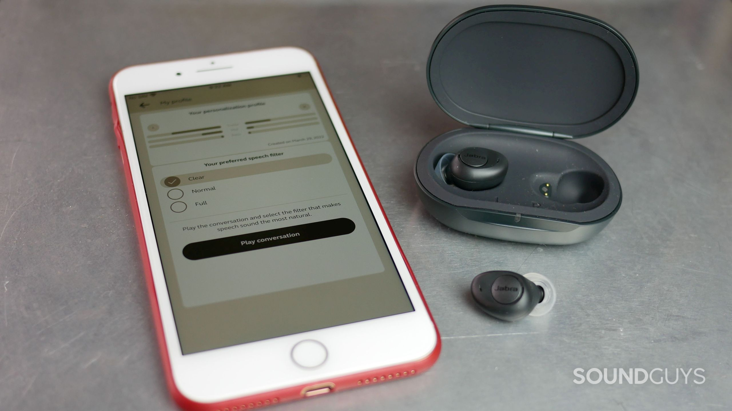 Jabra Enhance Plus earbuds and charging case with iPhone and Jabra Enhance app on personalization screen.