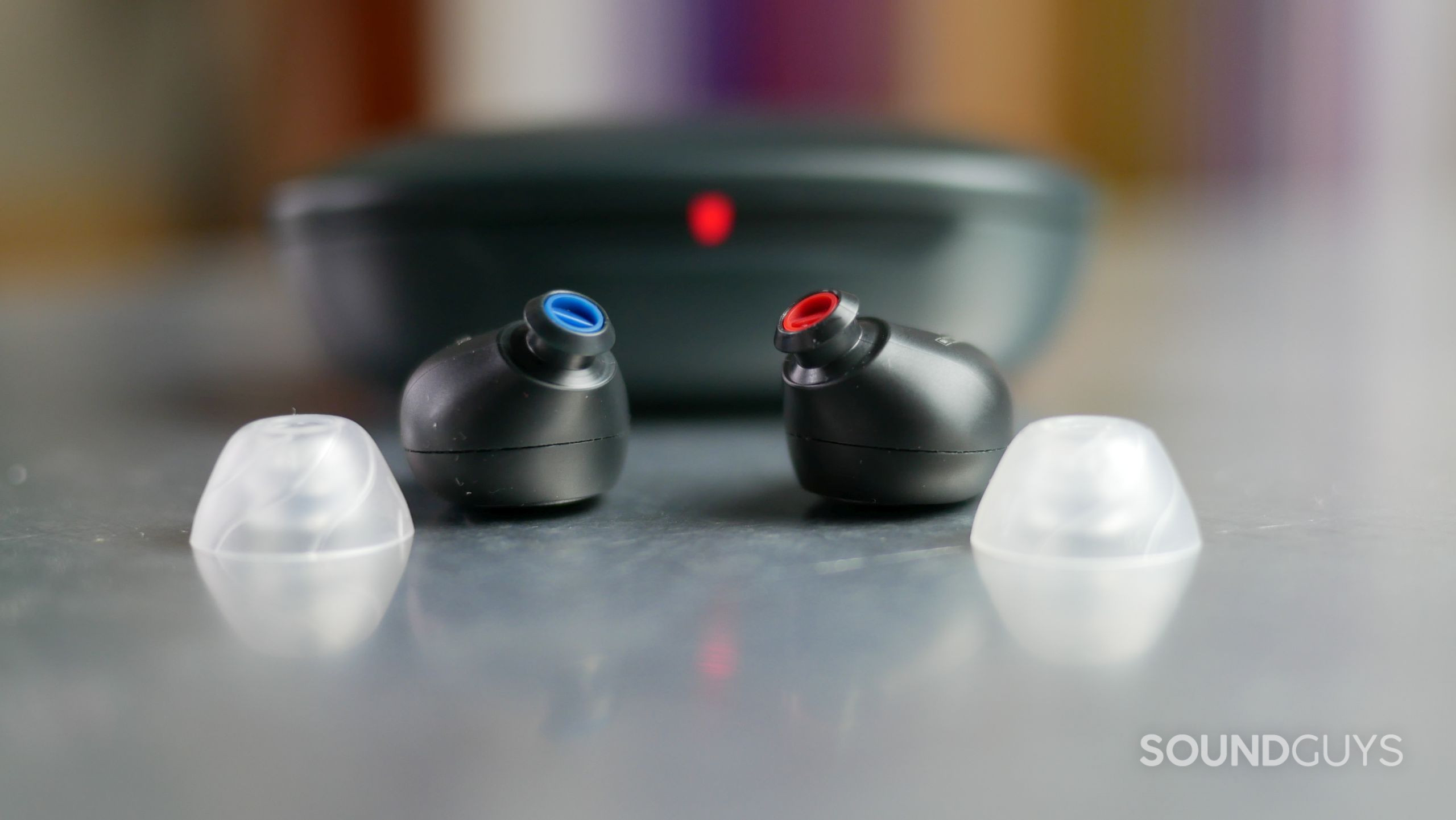 Jabra Enhance Plus Earbuds Closeup With Eartips in Foreground and Charging Case in Background Jabra Enhance Plus earbuds with silicone tips removed and charging case in background.