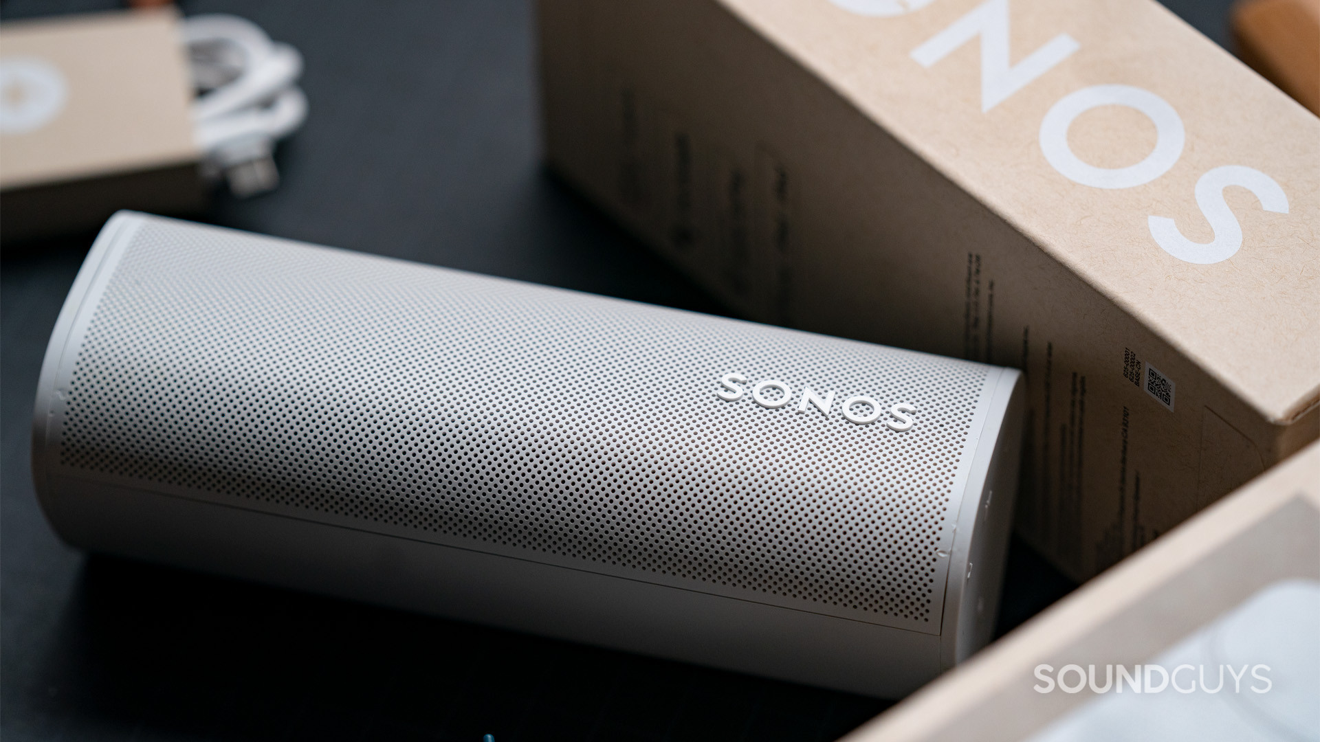 A Sonos Roam speaker sitting face-up next to the box it came in.
