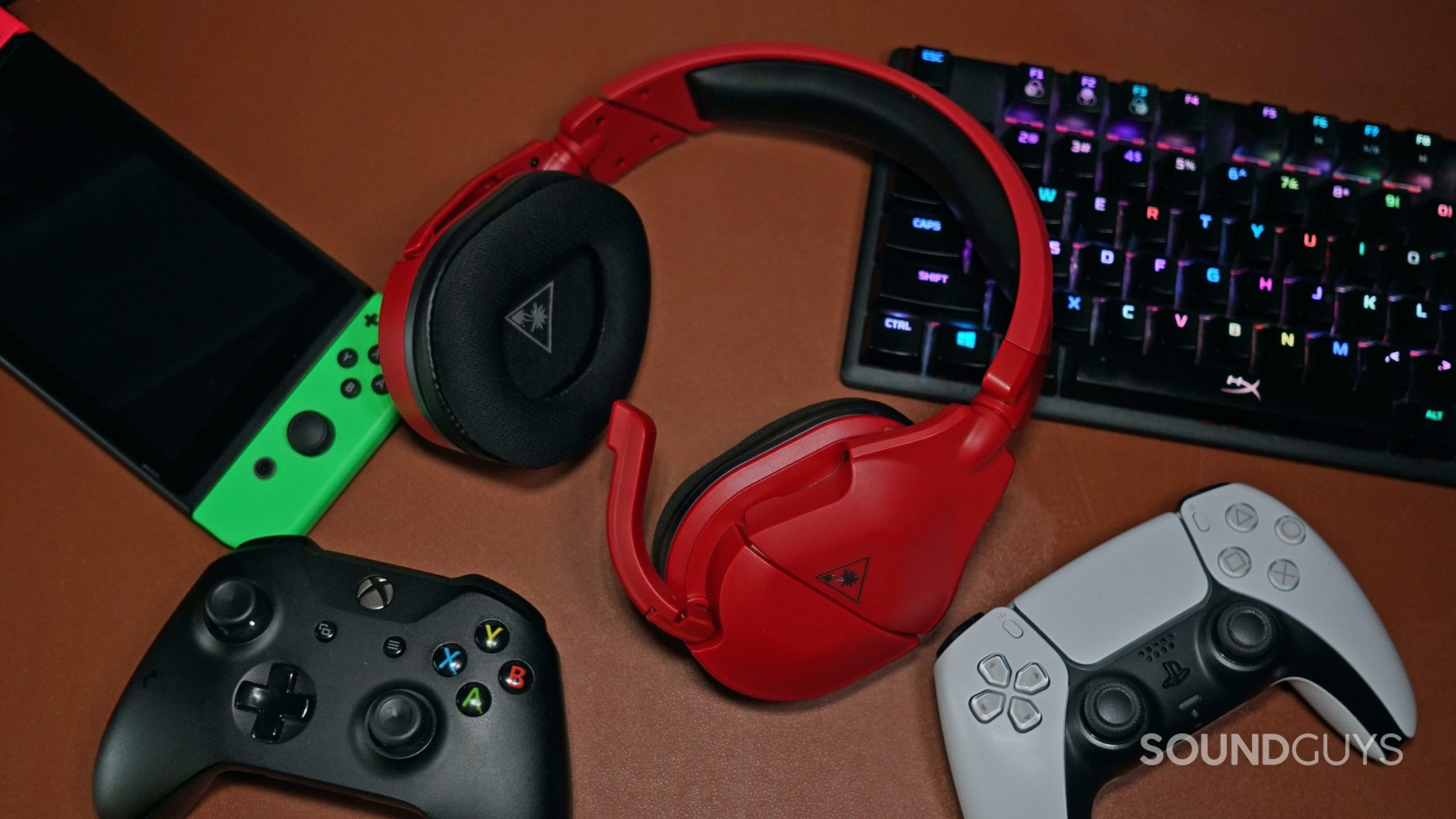 The Turtle Beach Stealth 600 Gen 2 MAX lays on a leather surface surrounded by a PlayStation DualShock controller, an Xbox One controller, a Nintendo Switch, and a HyperX mechanical gaming keyboard.