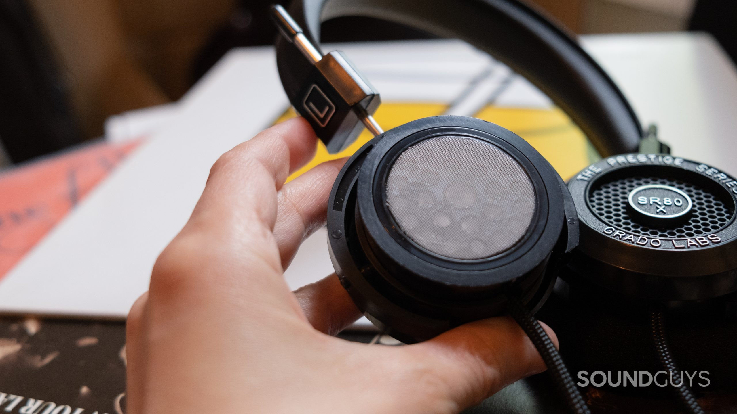 A hand holds the Grado Labs SR80x with the ear padding removed to show the driver.