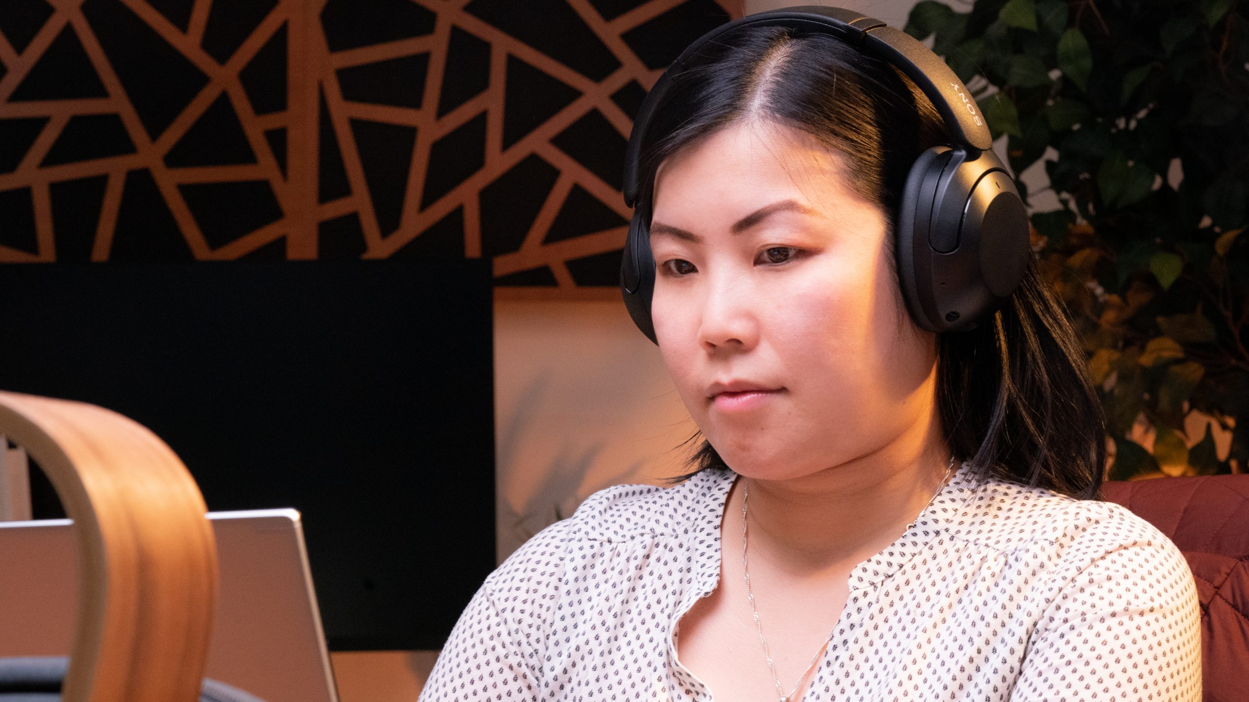 A woman faces slightly left looking at a laptop while wearing the Sony WH-XB910N.