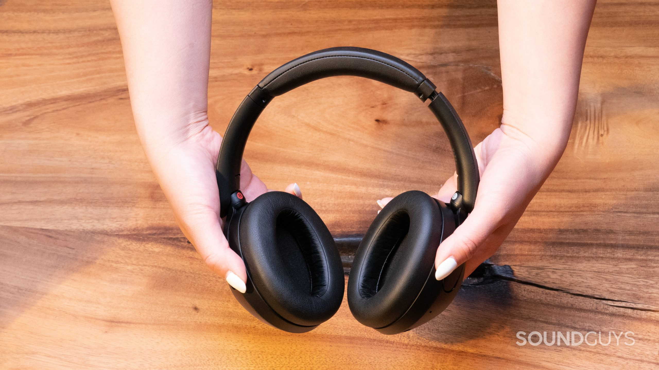 A set of hands holds the Sony WH-XB910N above a wood table