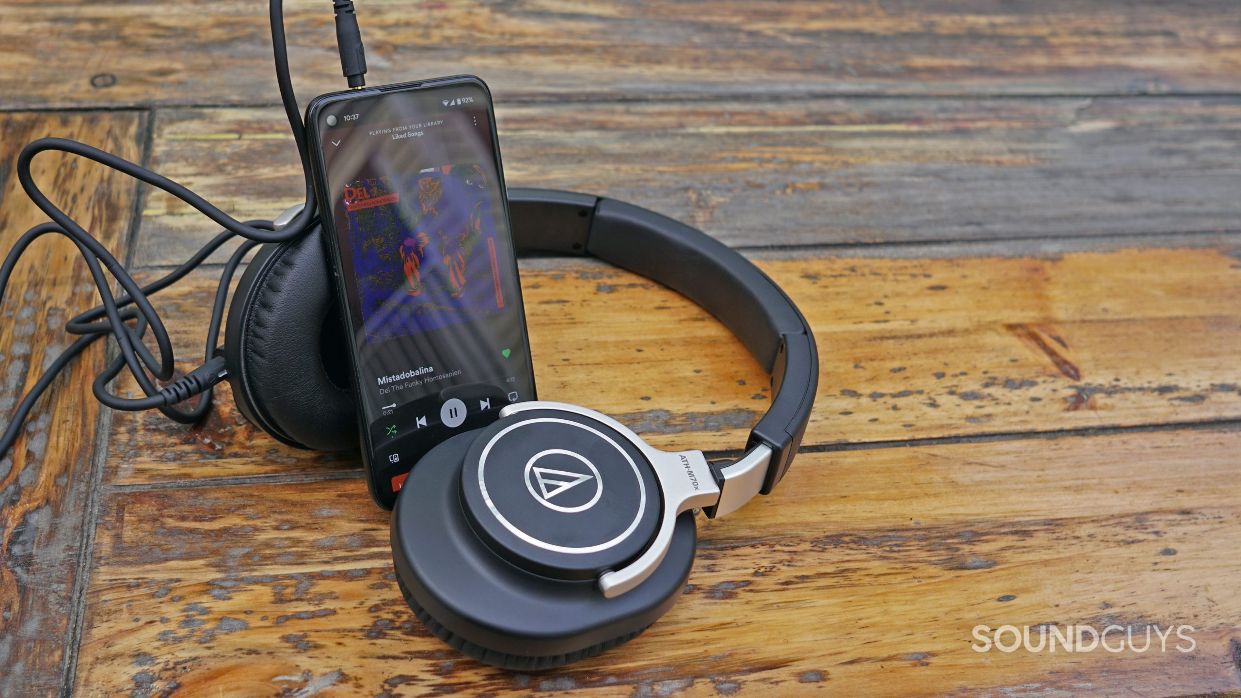 The Audio-Technica ATH-M70x lays on a wooden table plugged into a Pixel 4a running Spotify.
