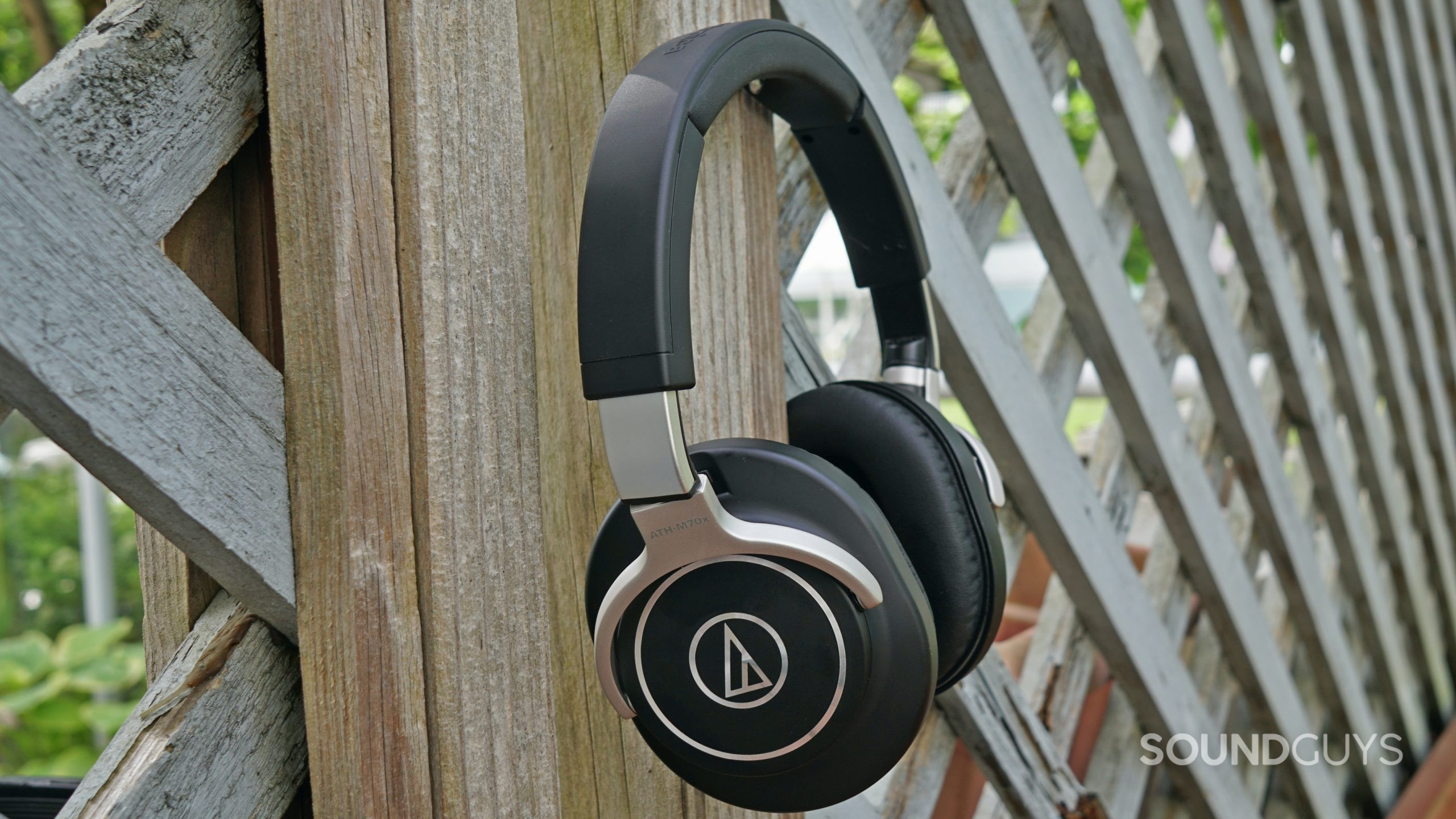 The Audio-Technica ATH-M70x hangs on a wooden lattice fence outside.