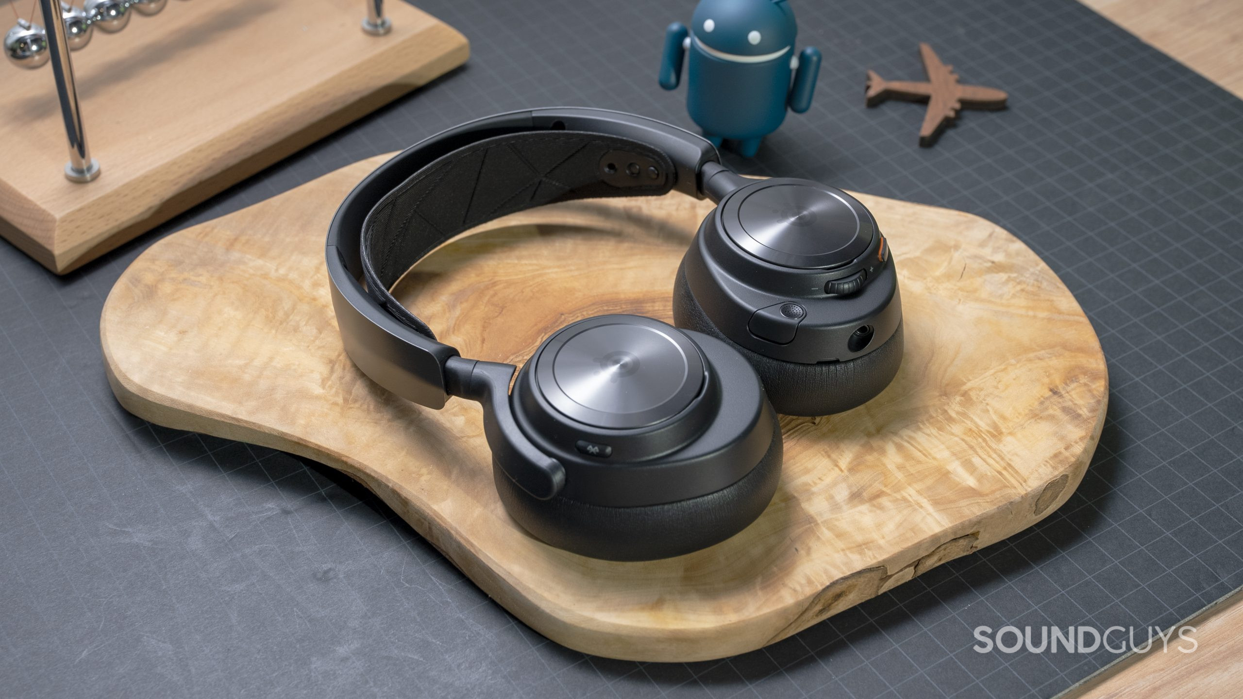 The SteelSeries Arctis Nova Pro Wireless laid flat on a wooden board atop a grey surface.