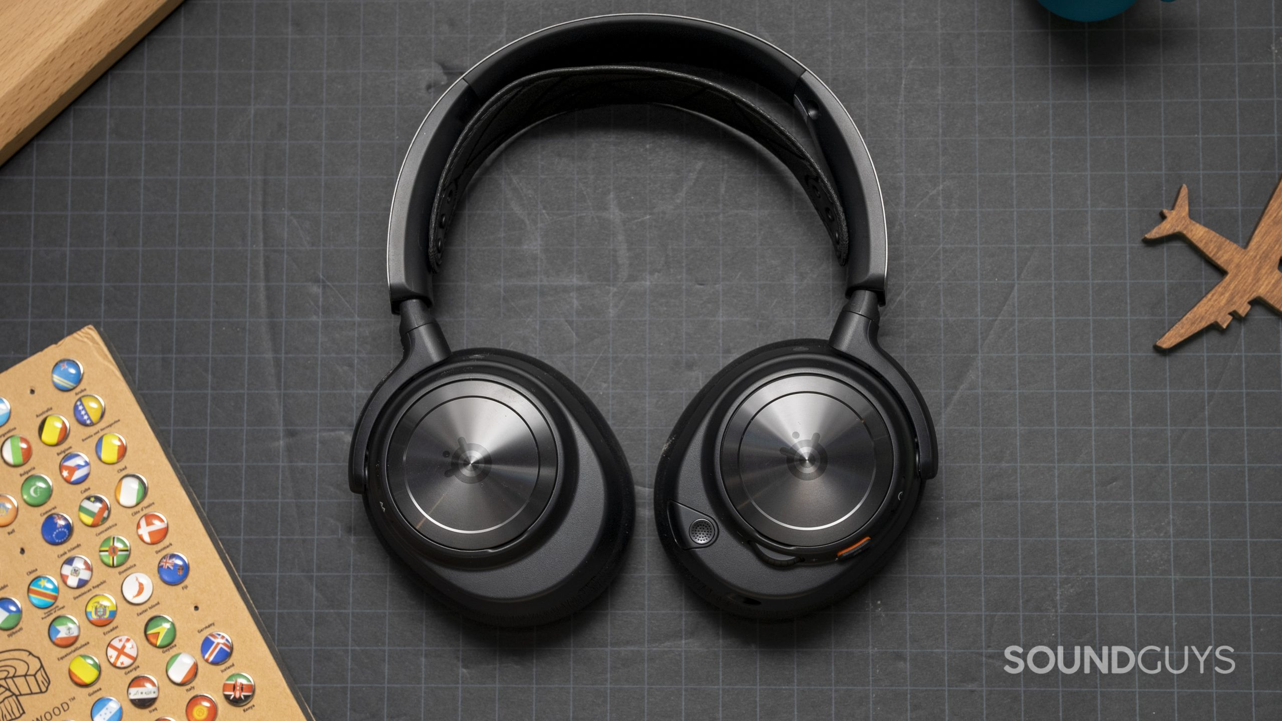 The SteelSeries Arctis Nova Pro Wireless laid flat on a grey surface next to a wooden board.