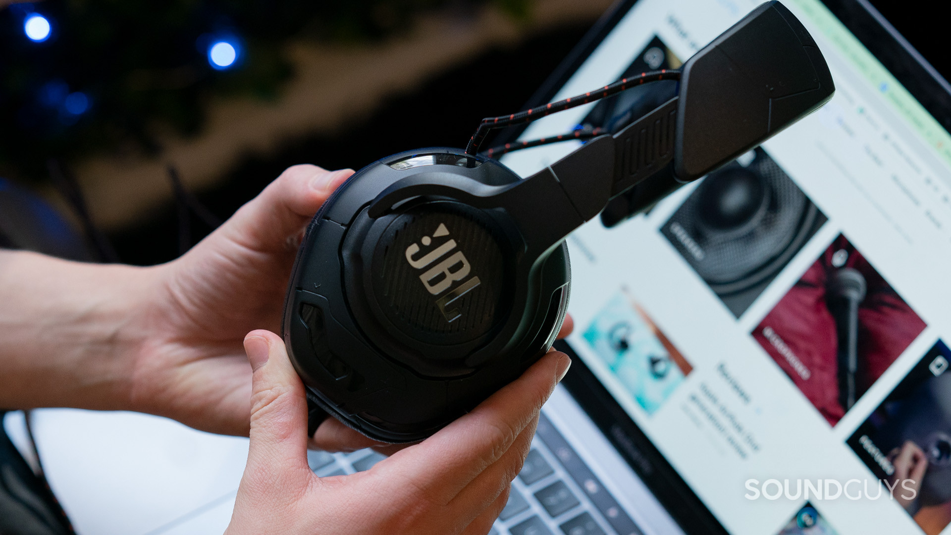 The JBL Quantum One being held in someone's hands with a laptop in the background