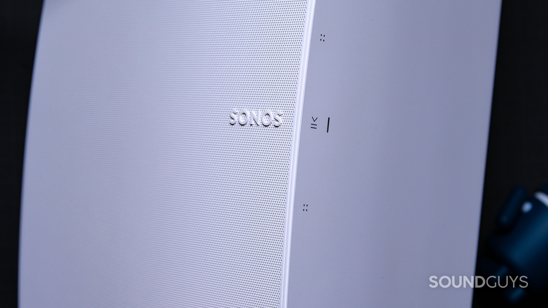 A white Sonos Five speaker showing a close-up of the Sonos logo and the contrl buttons. The speaker is oriented vertically.