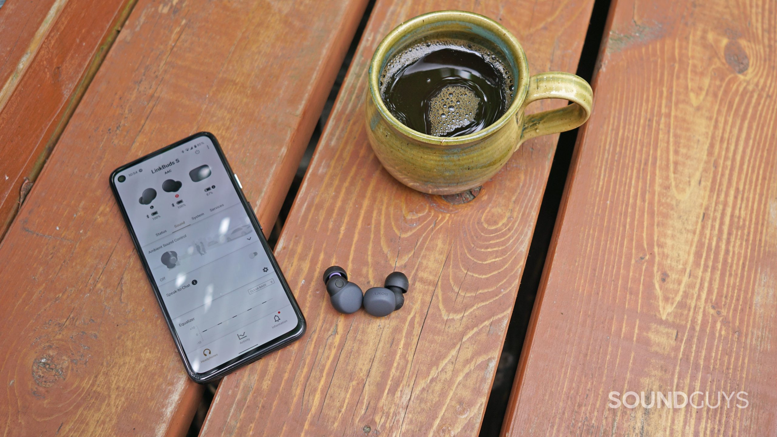 The Sony LinkBuds S true wireless earbuds lay on a wooden surface next to a google Pixel 4a running the Sony Headphones Connect app and a cup of coffee.