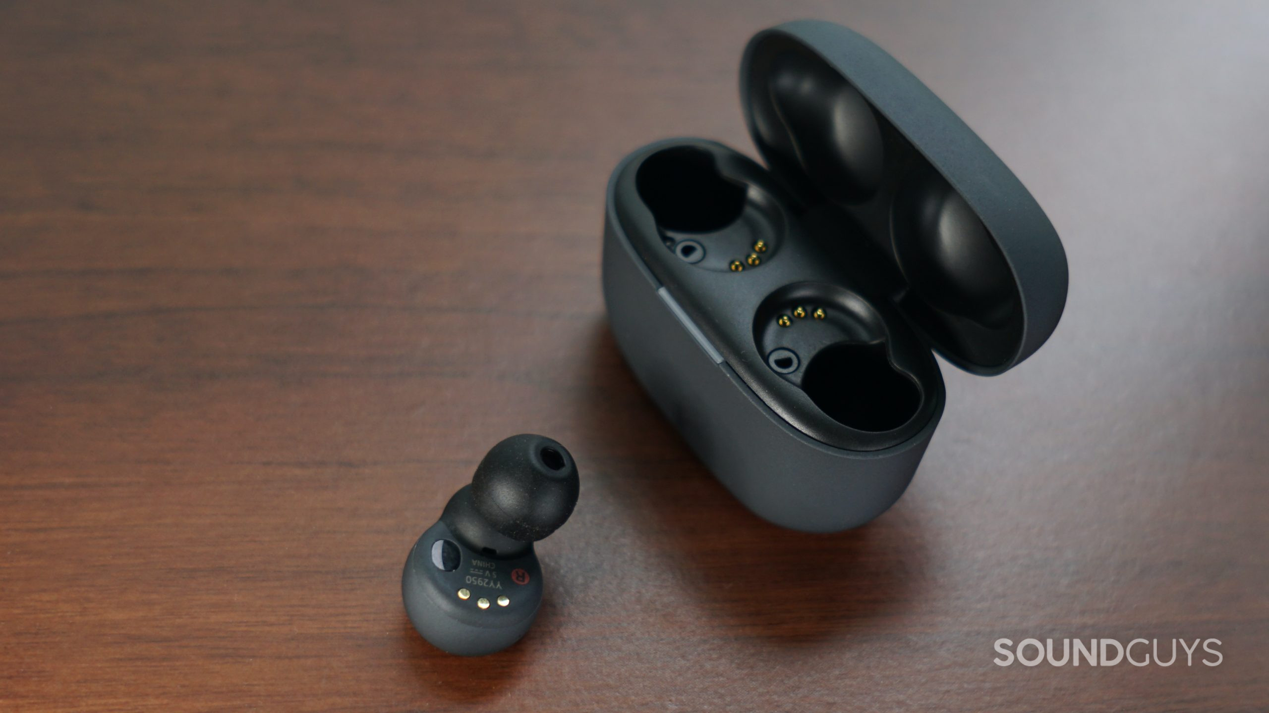 The Sony LinkBuds S lays on a wooden surface next to its open charging case.