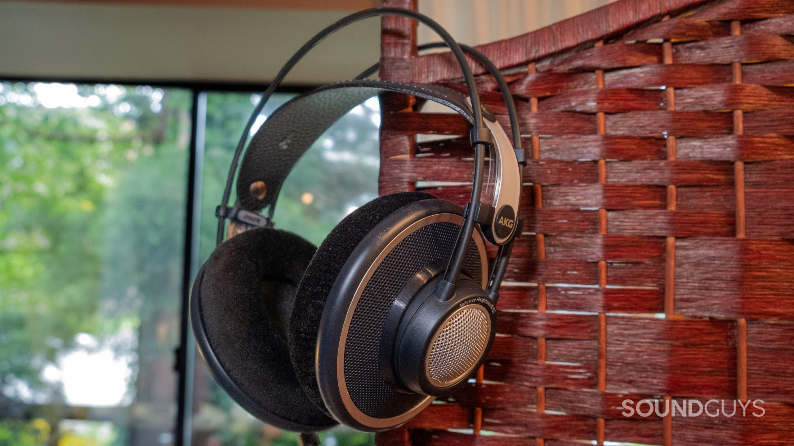 In the center of the image the AKG K702 hangs from a room divider with a window overlooking greenery in the background.